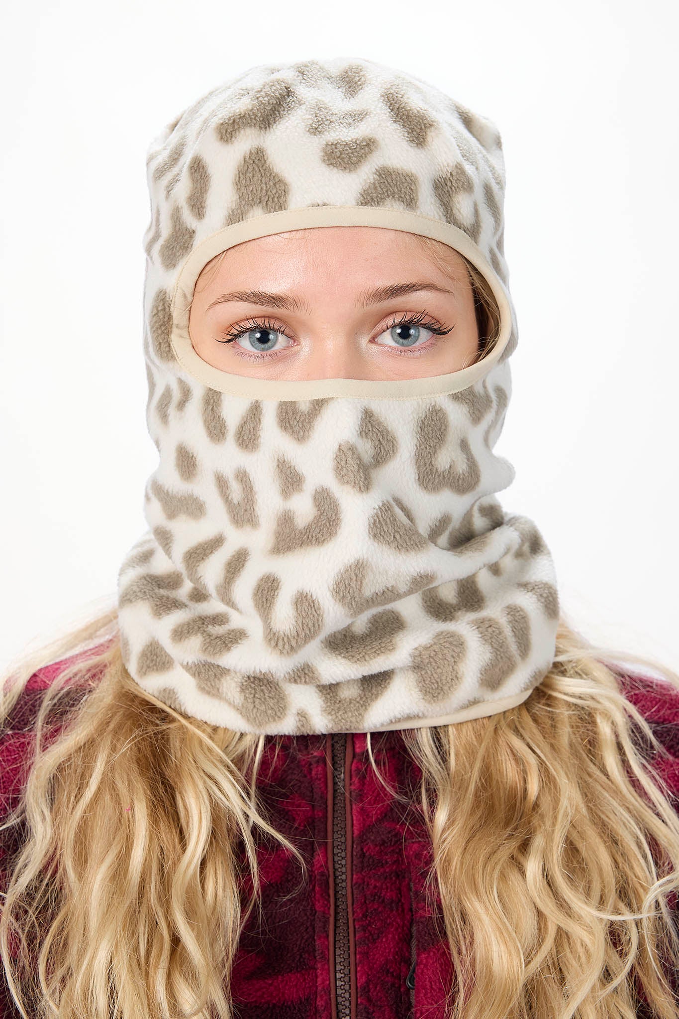 A woman wearing a white leopard patterned balaclava mask with a brown leopard print pattern, paired with an olive green hoodie against a plain white background.