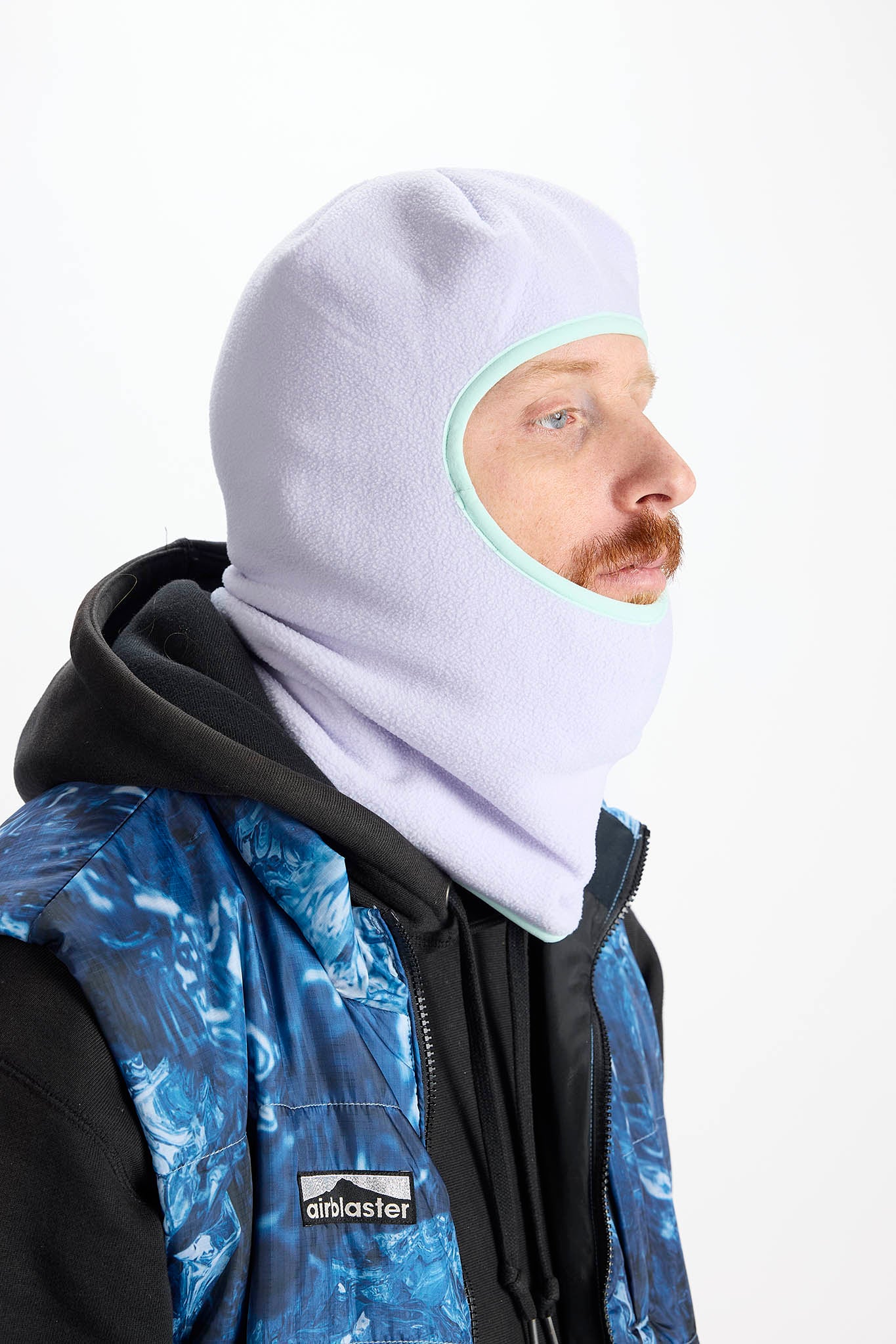 A man wearing a light purple balaclava mask with a brown leopard print pattern, paired with an olive green hoodie against a plain white background.