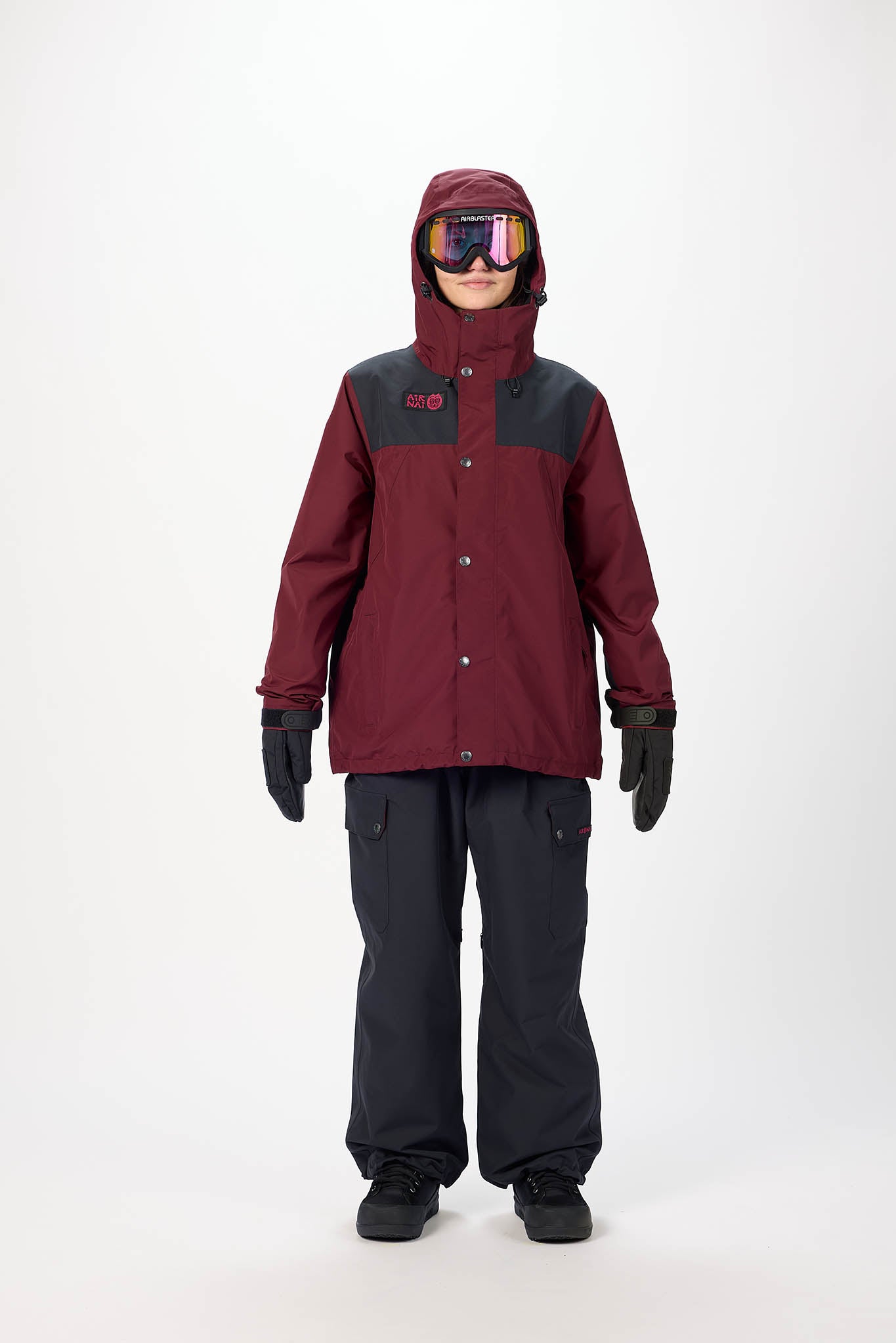 Person wearing a maroon and gray snowsuit with goggles on a white background