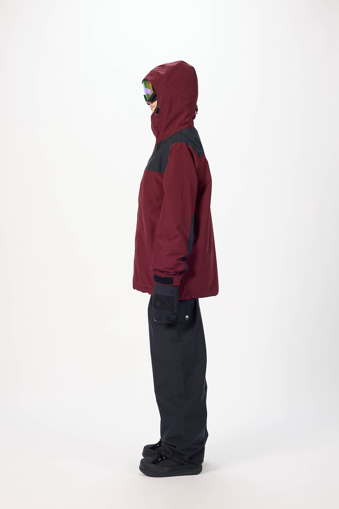 Person wearing a maroon and gray jacket with black pants on a white background