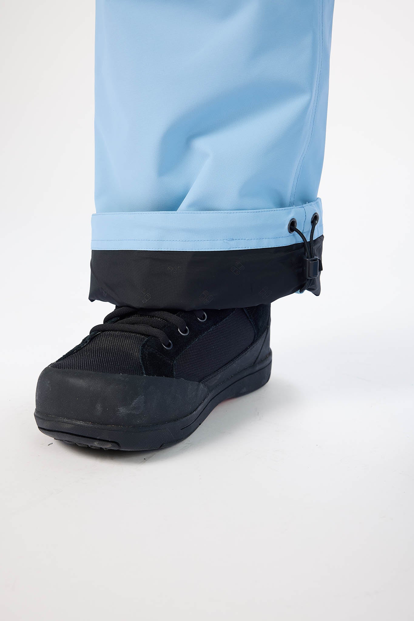 Black boot with a white sole on a light blue pant leg against a white background