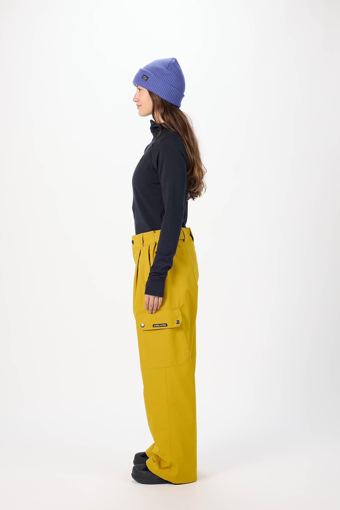 Person wearing a dark jacket, yellow pants, and a purple beanie on a white background