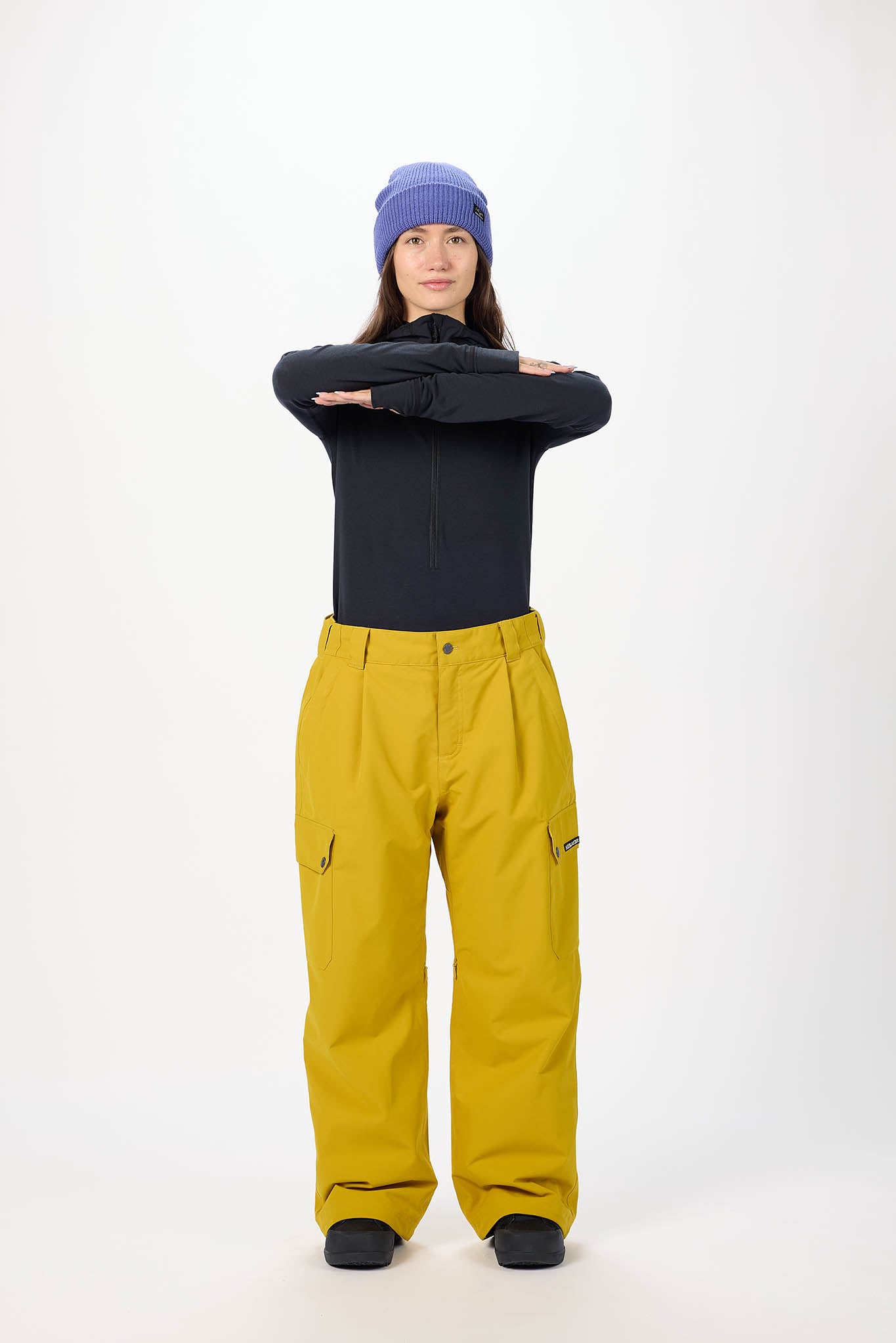Person wearing a black top, yellow pants, and a blue beanie on a white background
