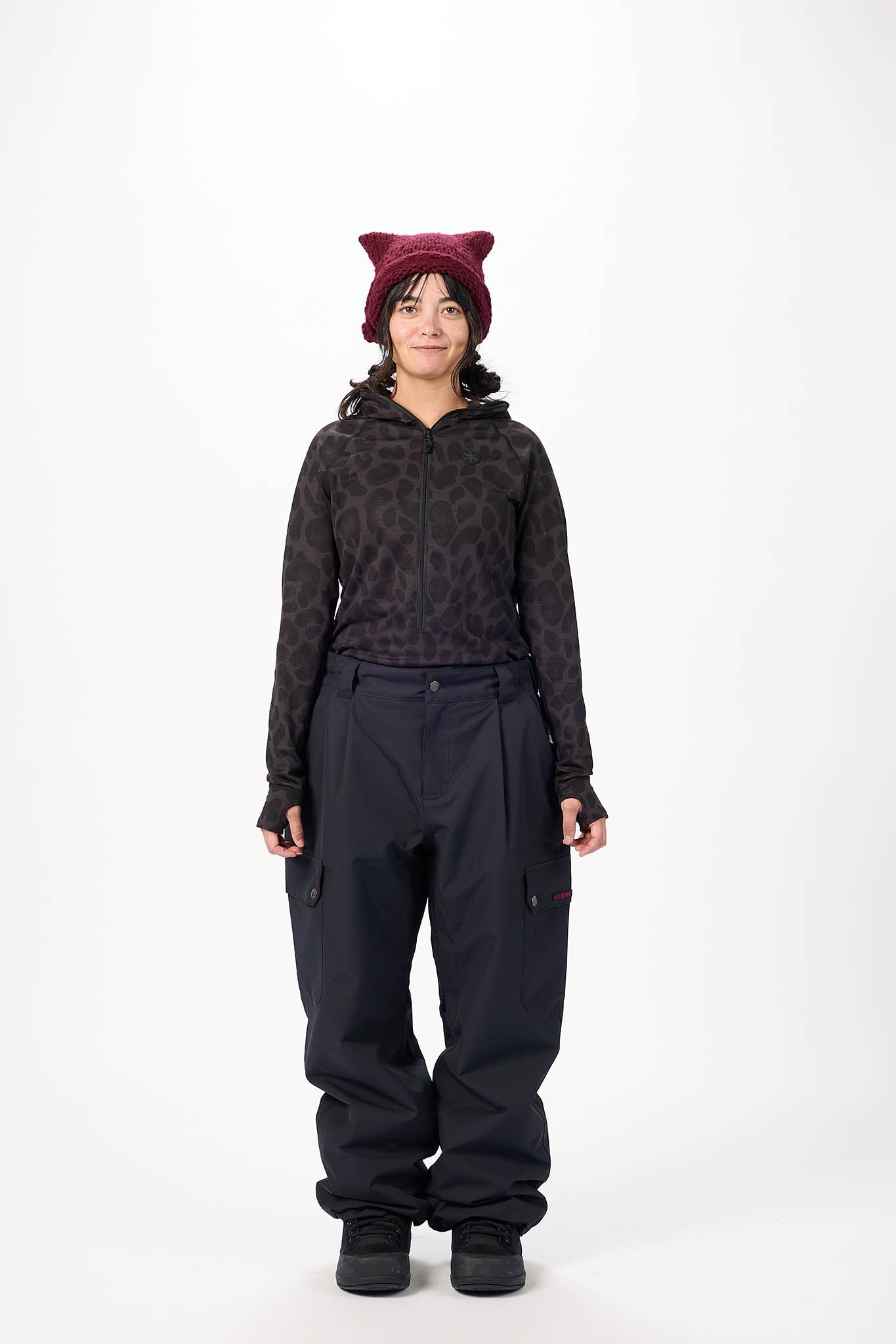 Person wearing a patterned hoodie and black pants with a maroon beanie on a white background
