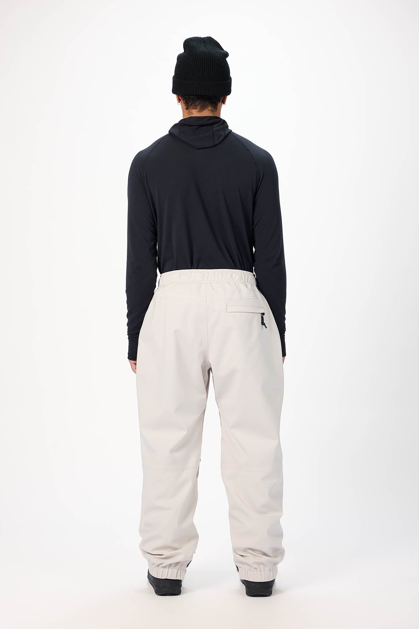 Person wearing a black long-sleeve shirt and beige pants on a white background