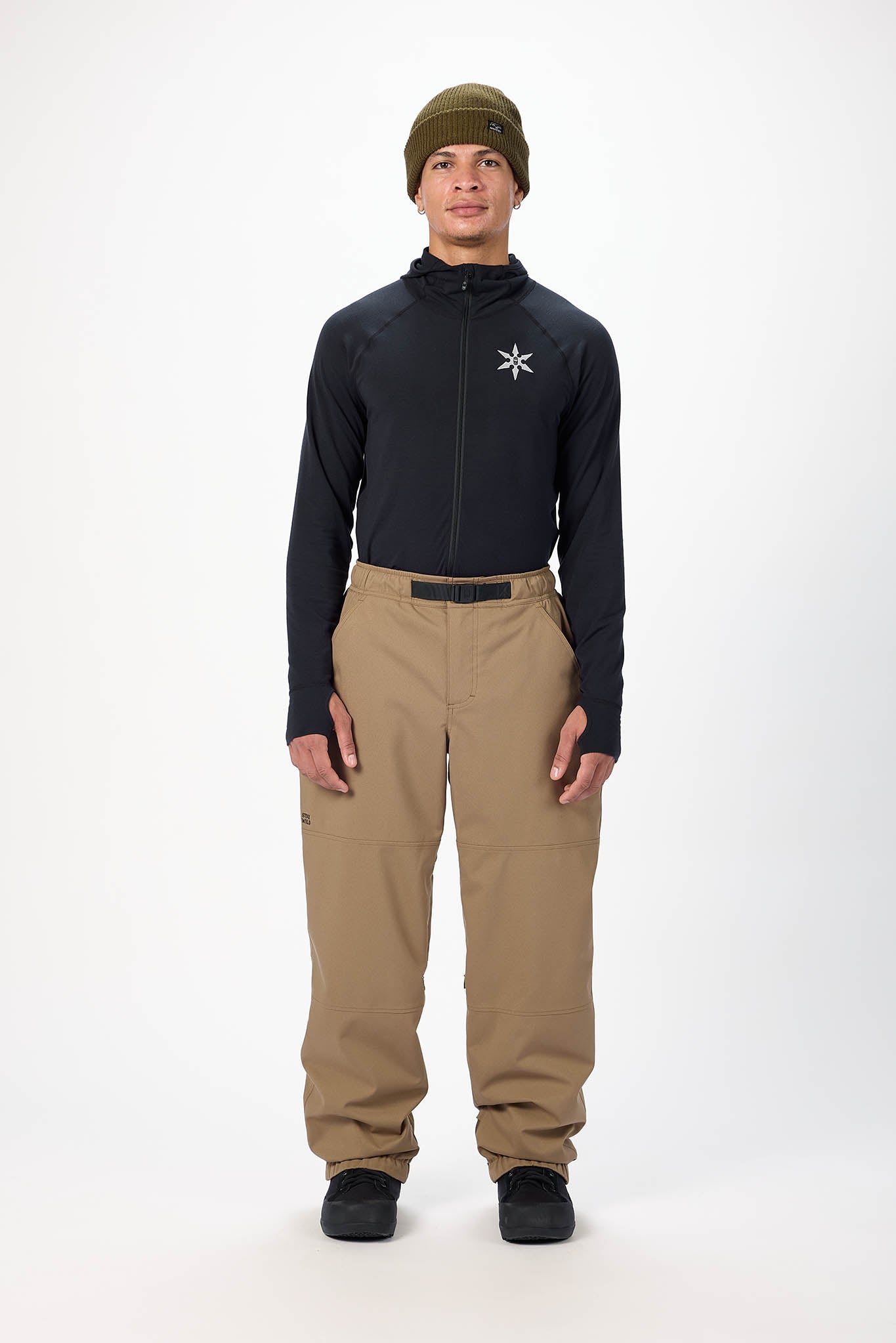 Person wearing a black jacket with a logo and beige pants on a white background
