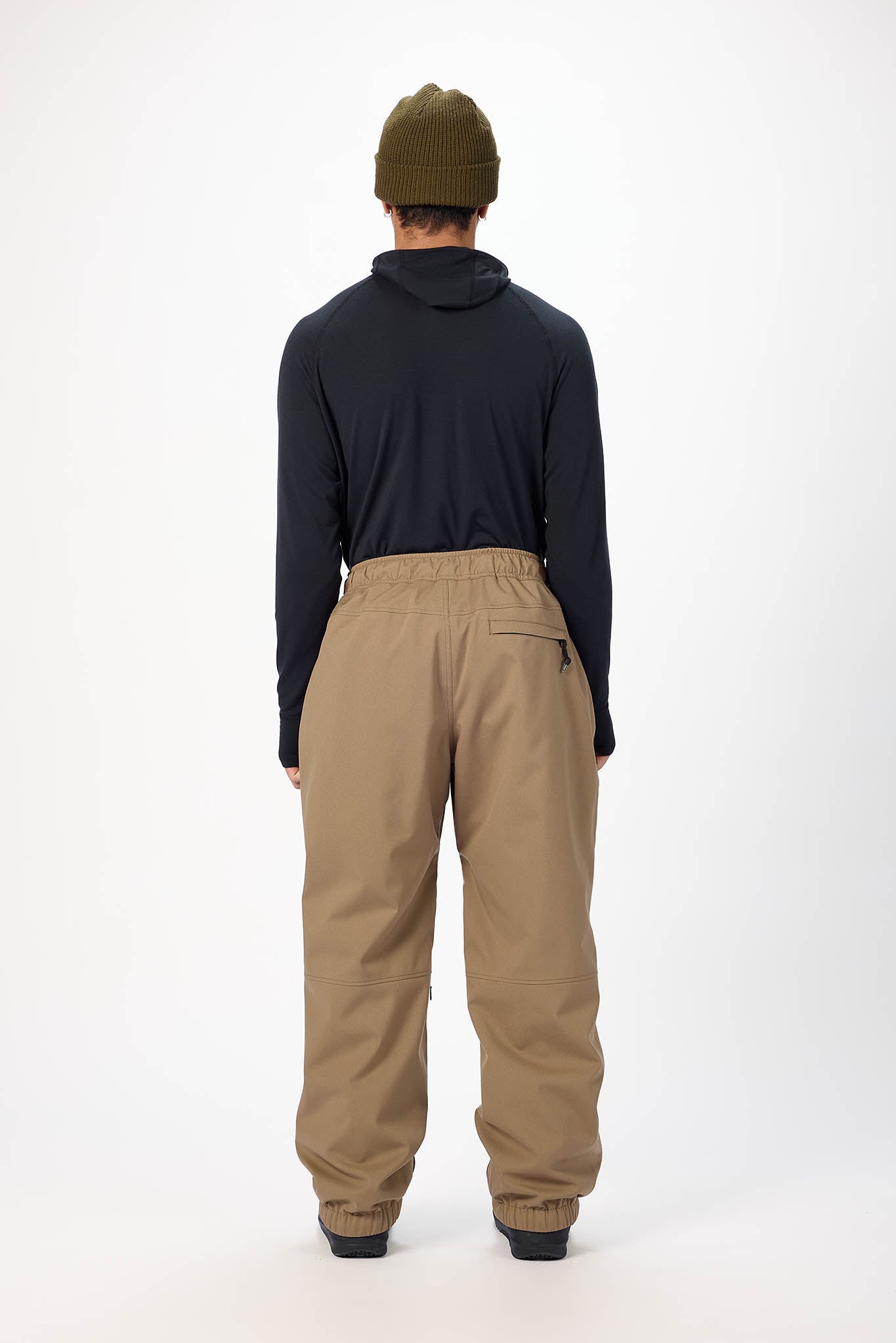 Person wearing a black jacket and beige pants on a white background