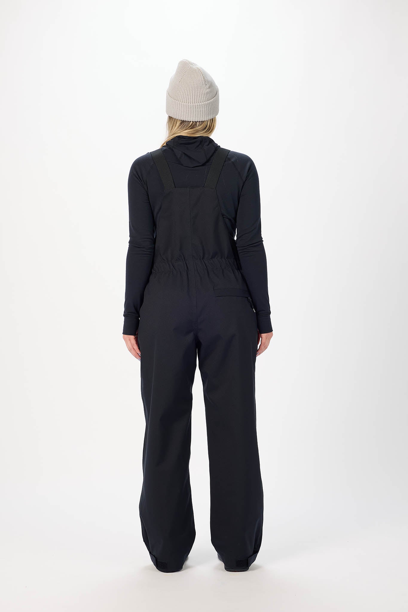 Person wearing a black jumpsuit and beige beanie on a white background