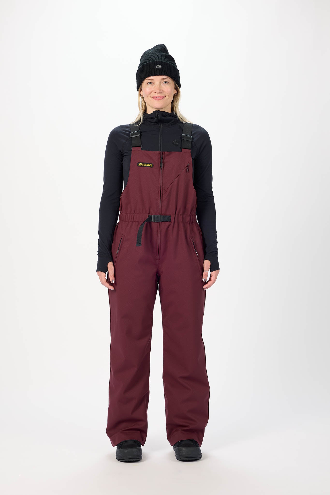 Person wearing maroon bib overalls and black jacket on a white background
