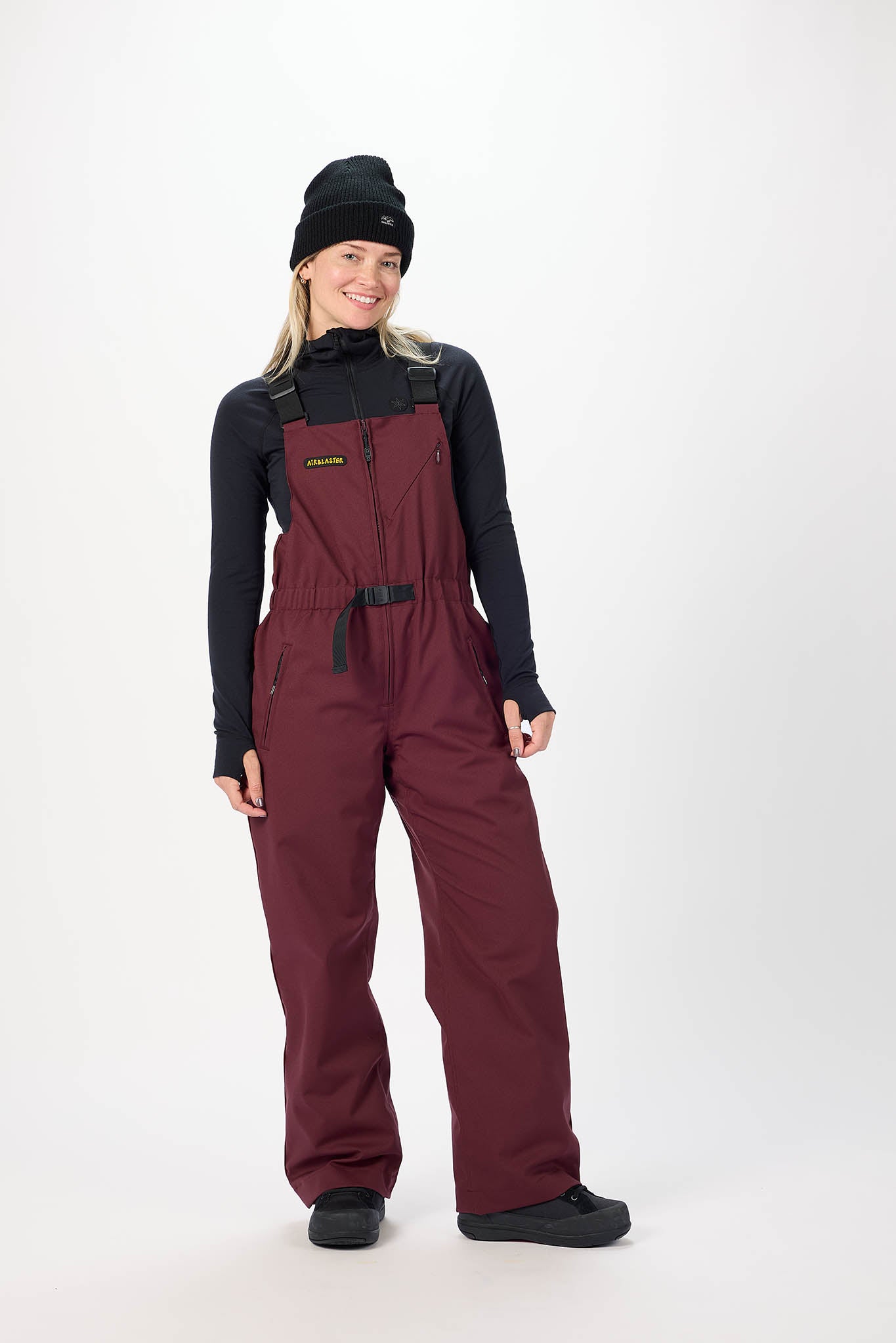 Person wearing a maroon snow bib overalls with a black top on a white background