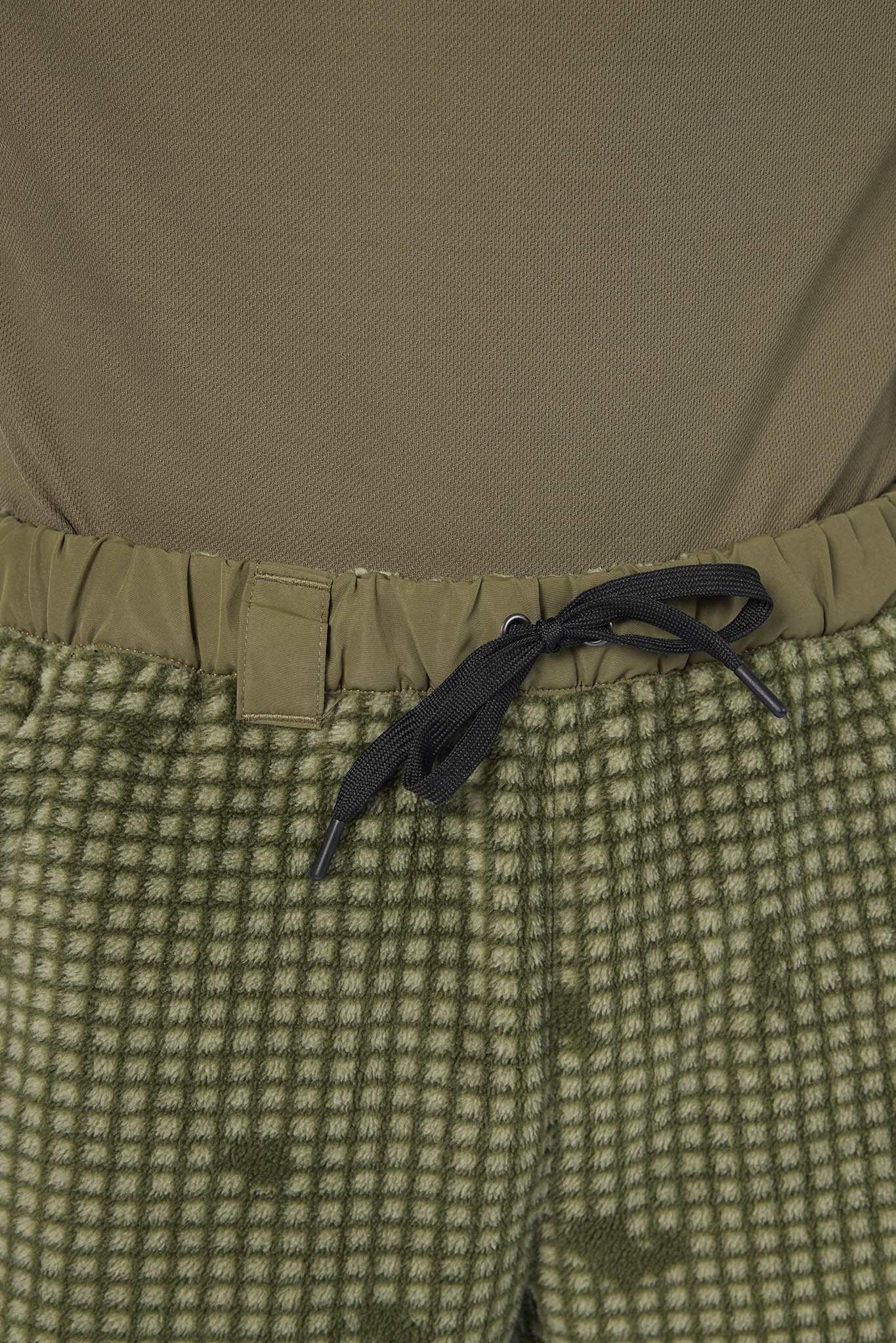 Close-up of a person wearing olive green patterned pants with a black drawstring and a solid olive top.