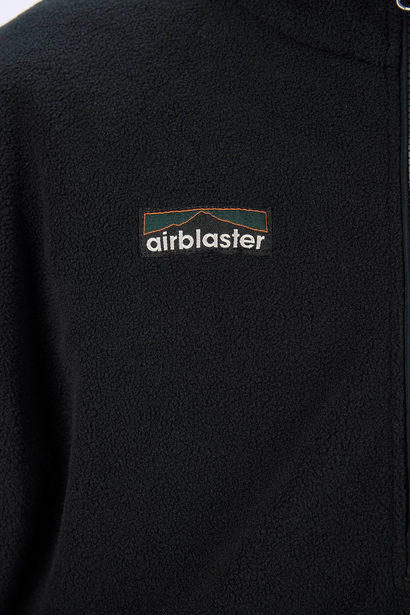 Close-up of a black fleece pullover jacket with a small embroidered Airblaster logo on the chest.