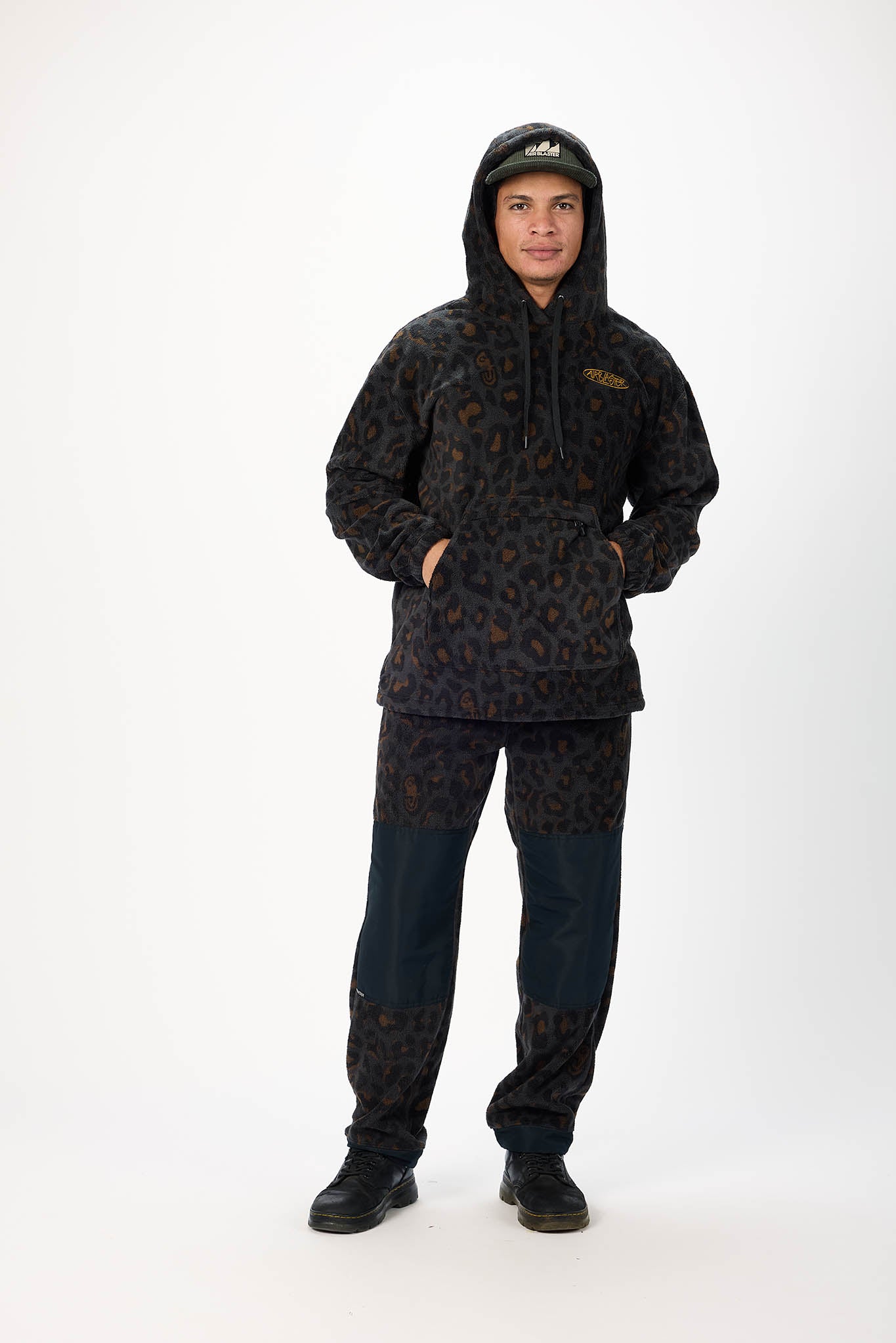 A model wearing a matching dark patterned fleece hoodie and pants set with dark blue denim lower legs, standing against a plain white studio background.