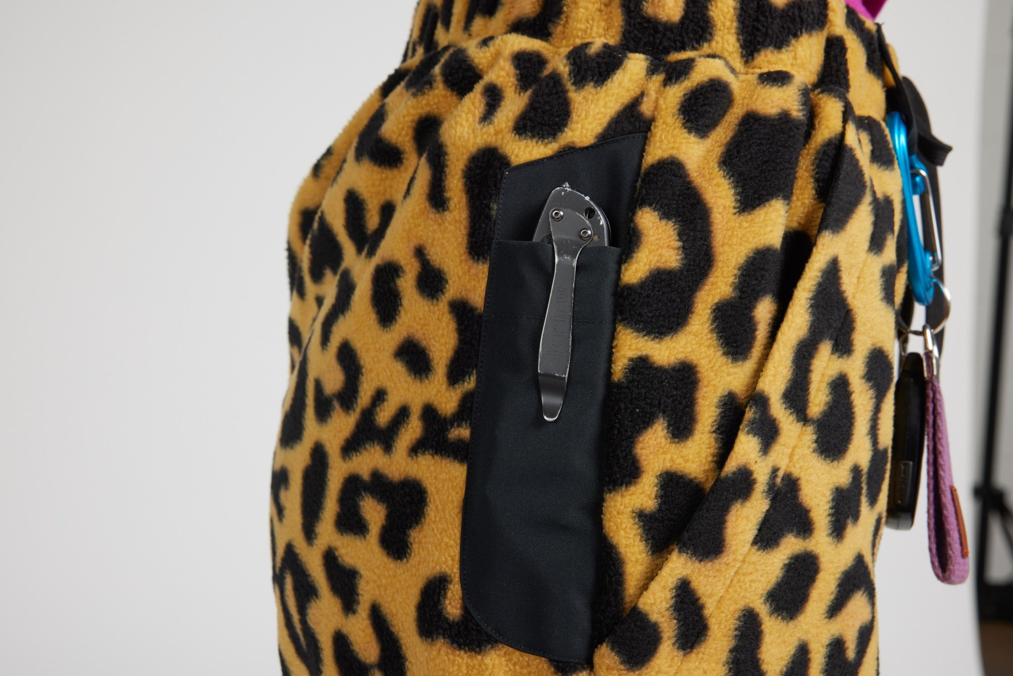 Close-up of a leopard-print fleece bag with a black side pocket holding a silver knife, shown against a plain light background.