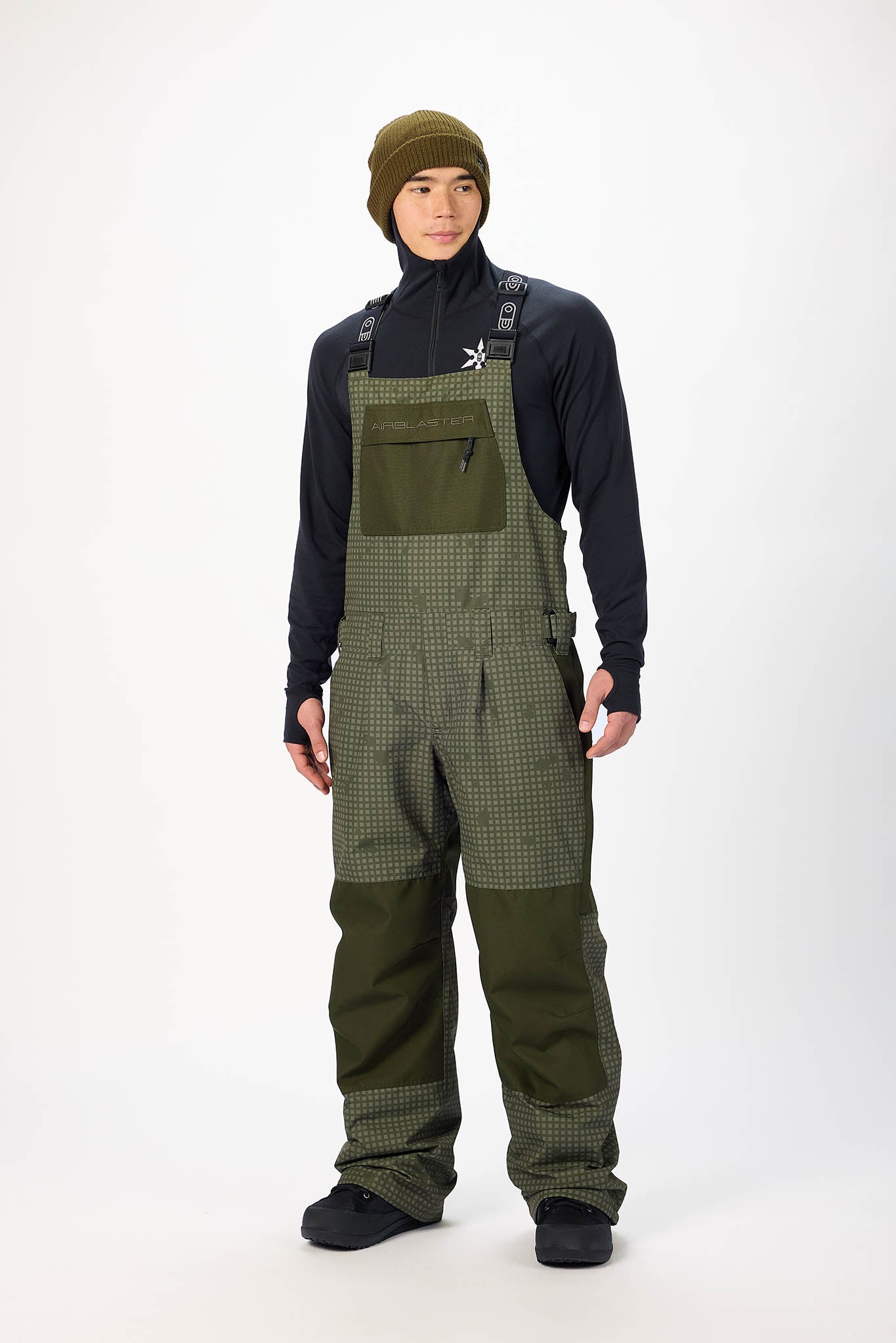 Person wearing green checkered bib overalls and a dark jacket on a white background