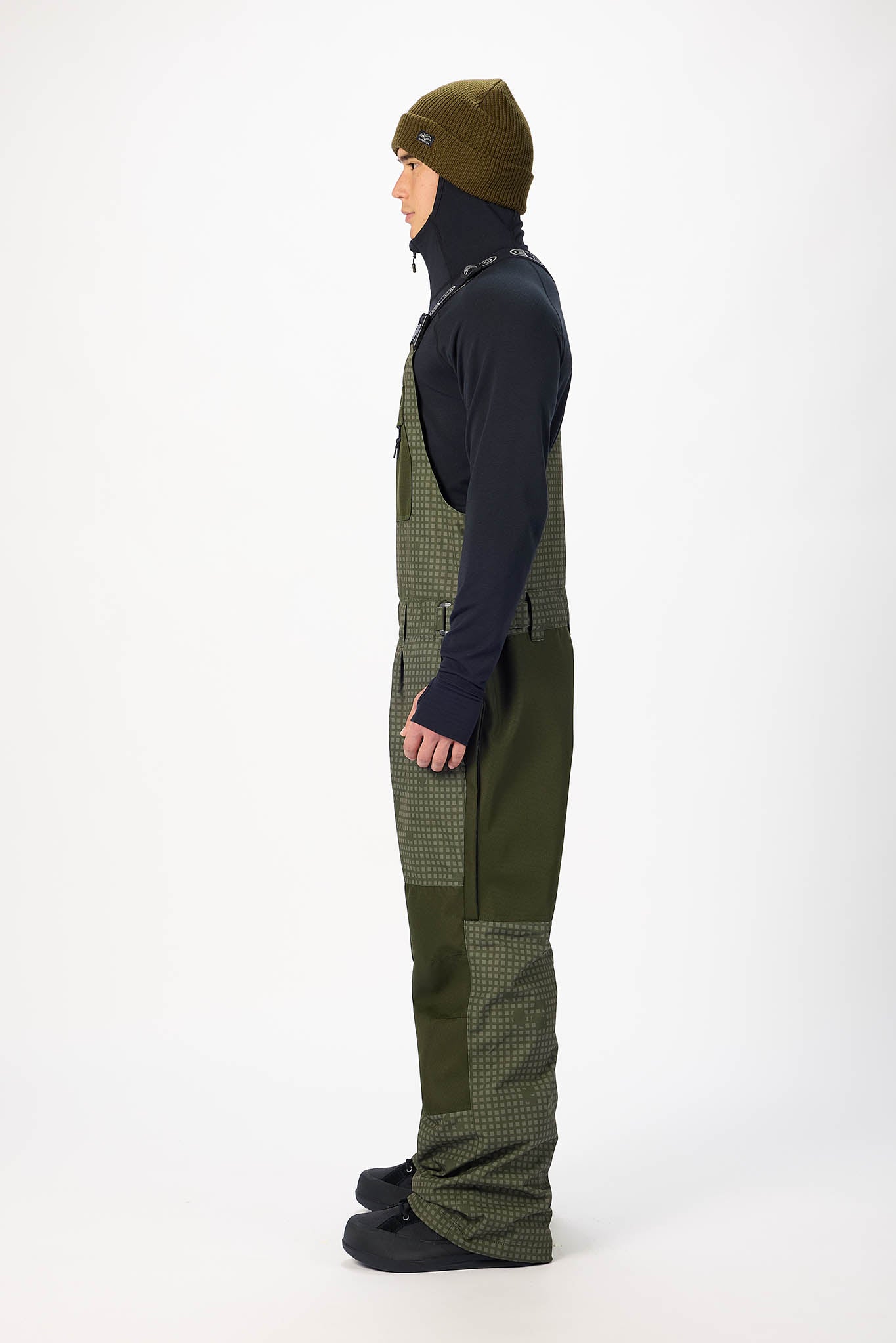 Person wearing a dark jacket, green checkered pants, and a matching beanie on a white background
