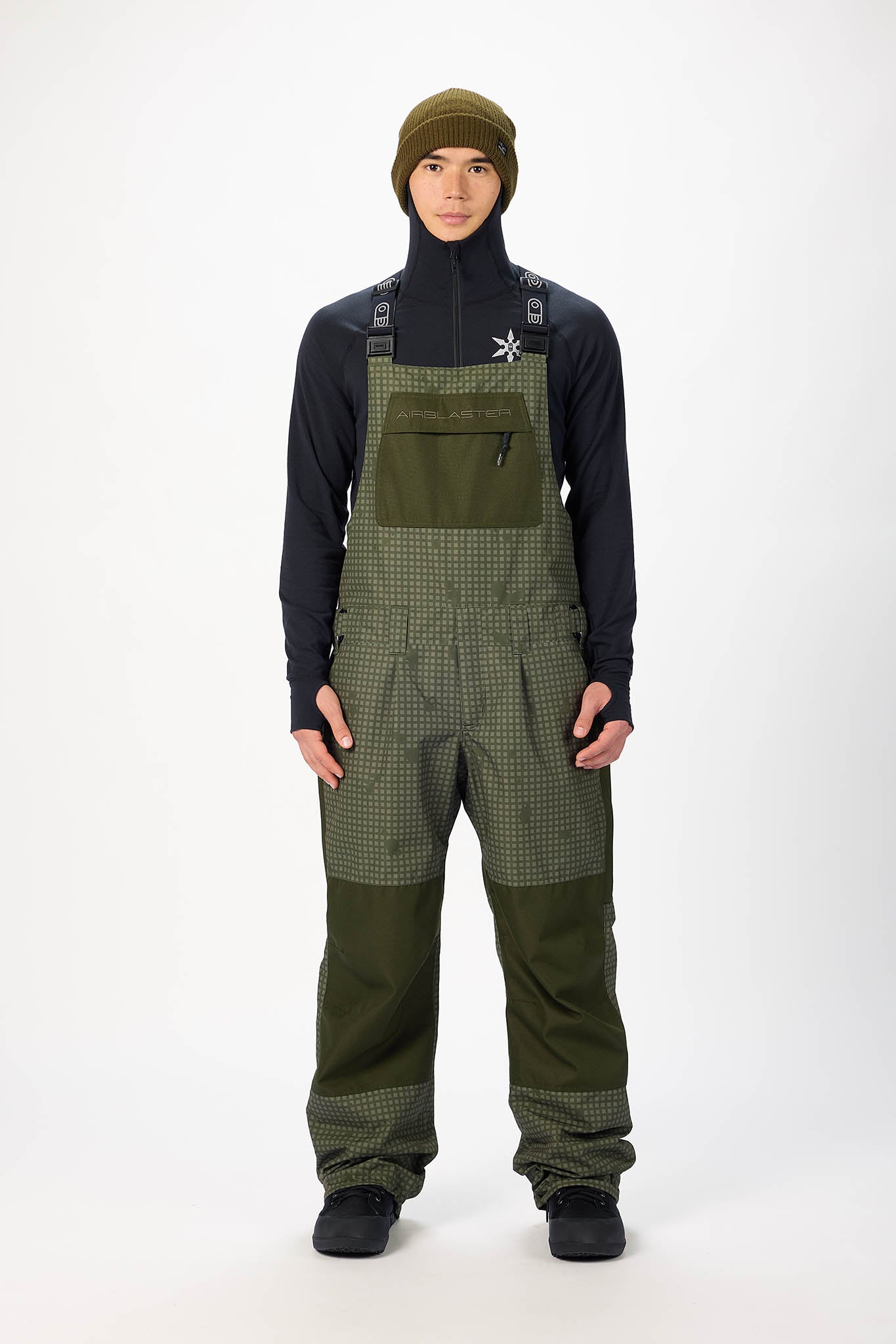 Person wearing green checkered bib overalls with a black shirt on a white background