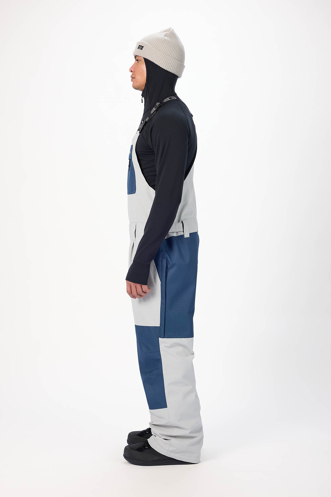 Person wearing a dark jacket, light gray pants, and a white beanie on a white background