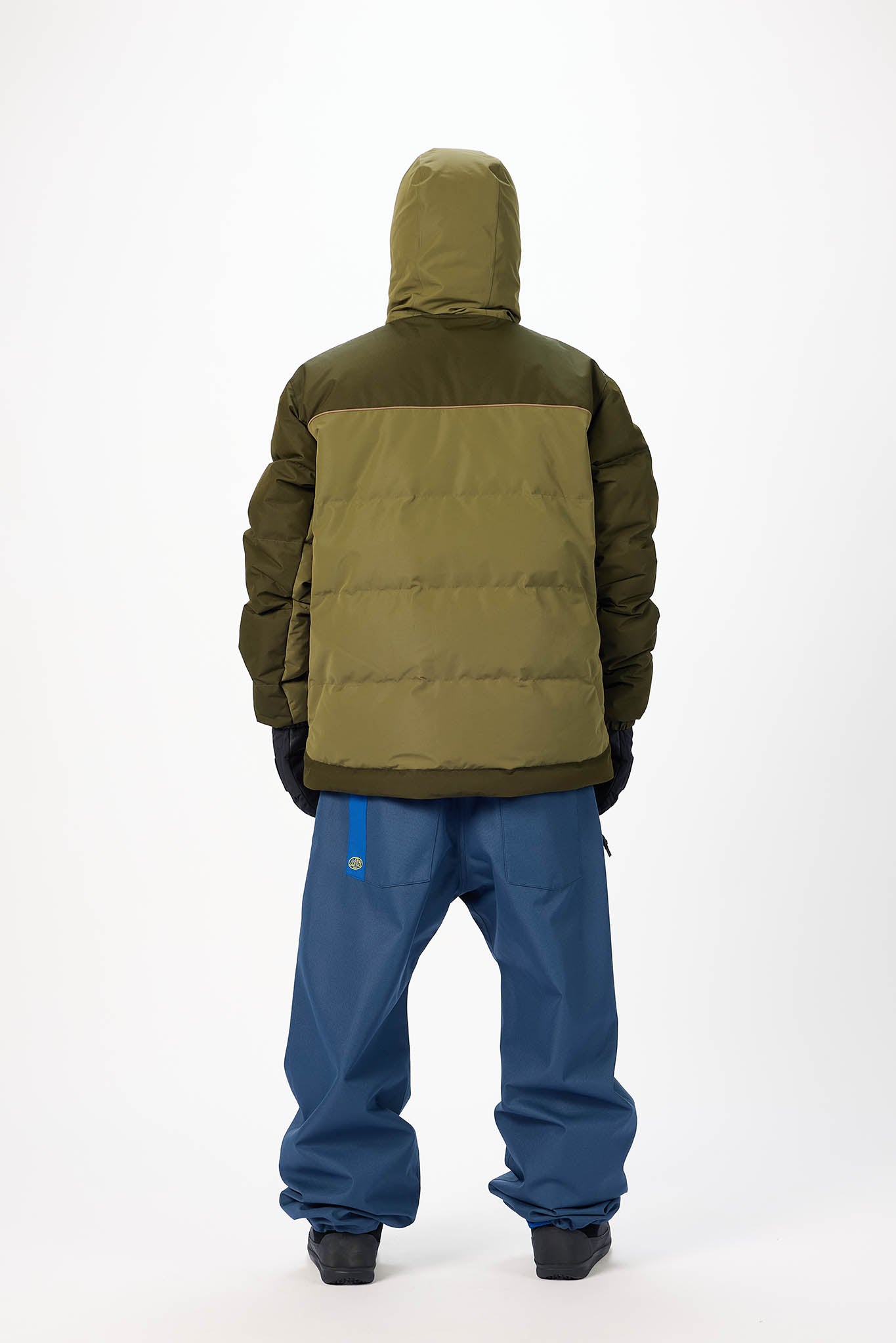 Person wearing a green and brown insulated jacket with blue pants on a white background