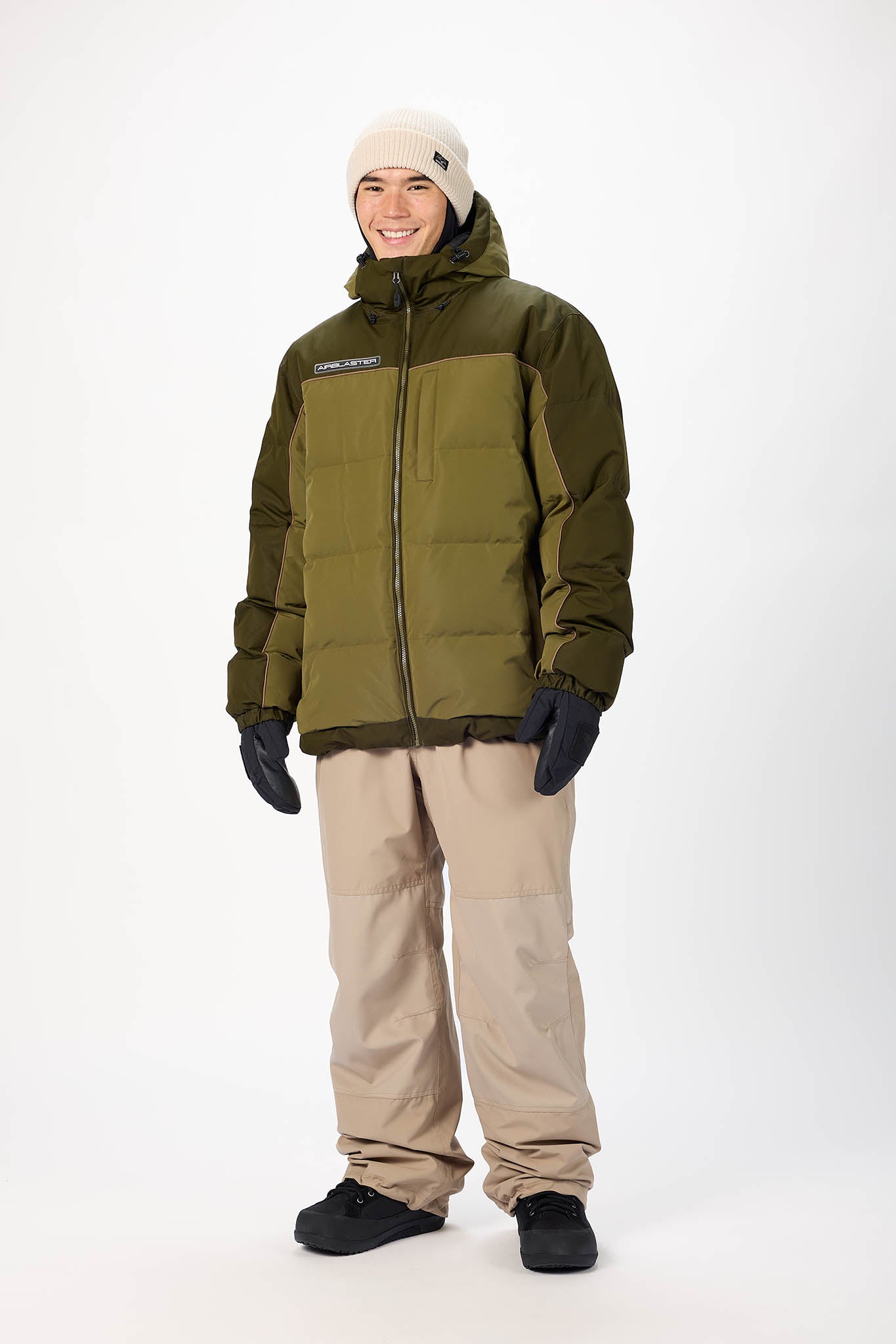 Person wearing an olive green puffer jacket, beige pants, and black gloves on a white background