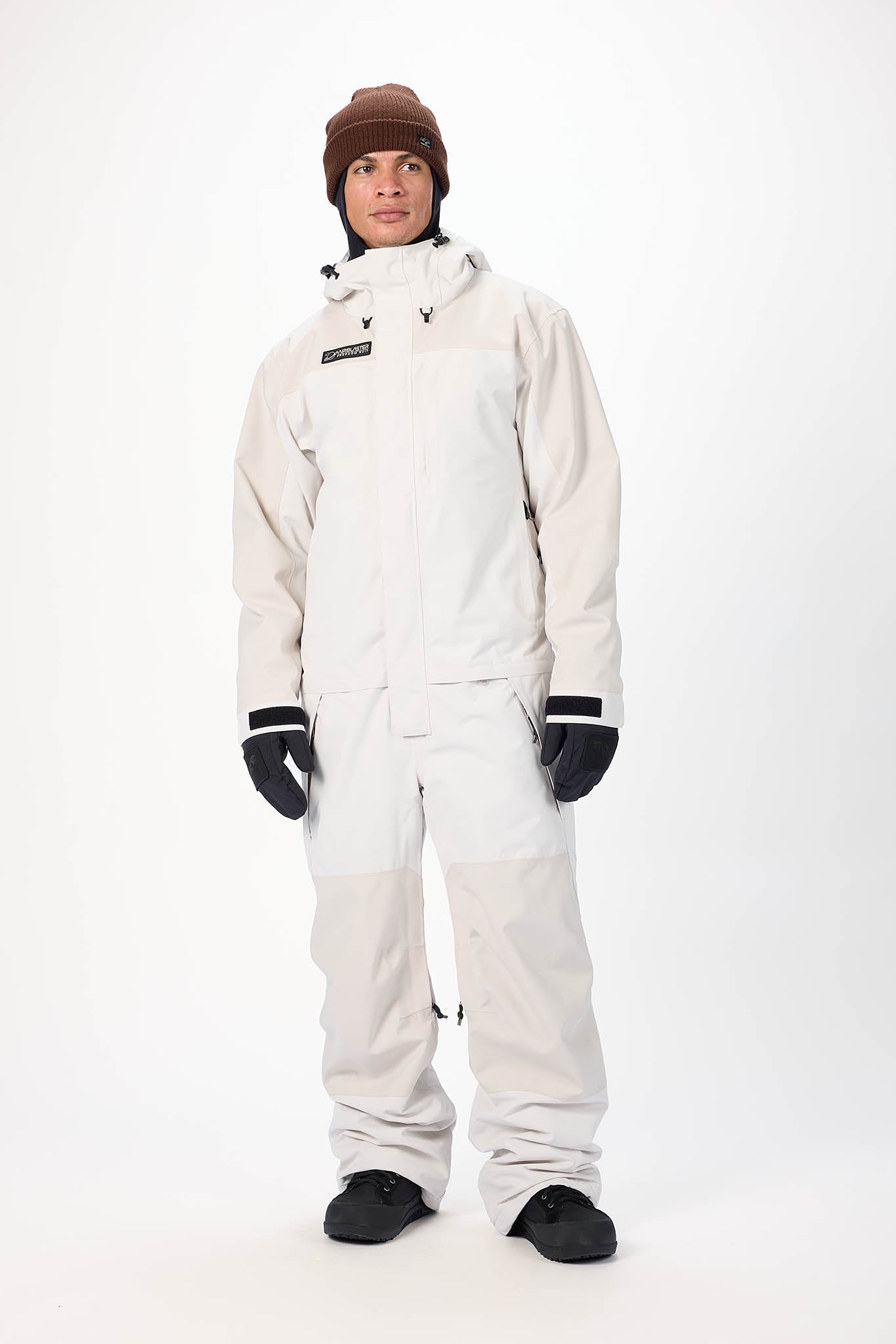Person wearing a white snowsuit with black gloves and boots on a white background