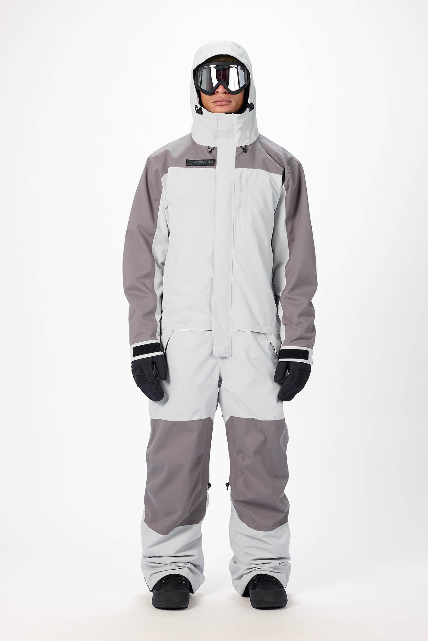 Person wearing a gray and white snowsuit with goggles on a white background