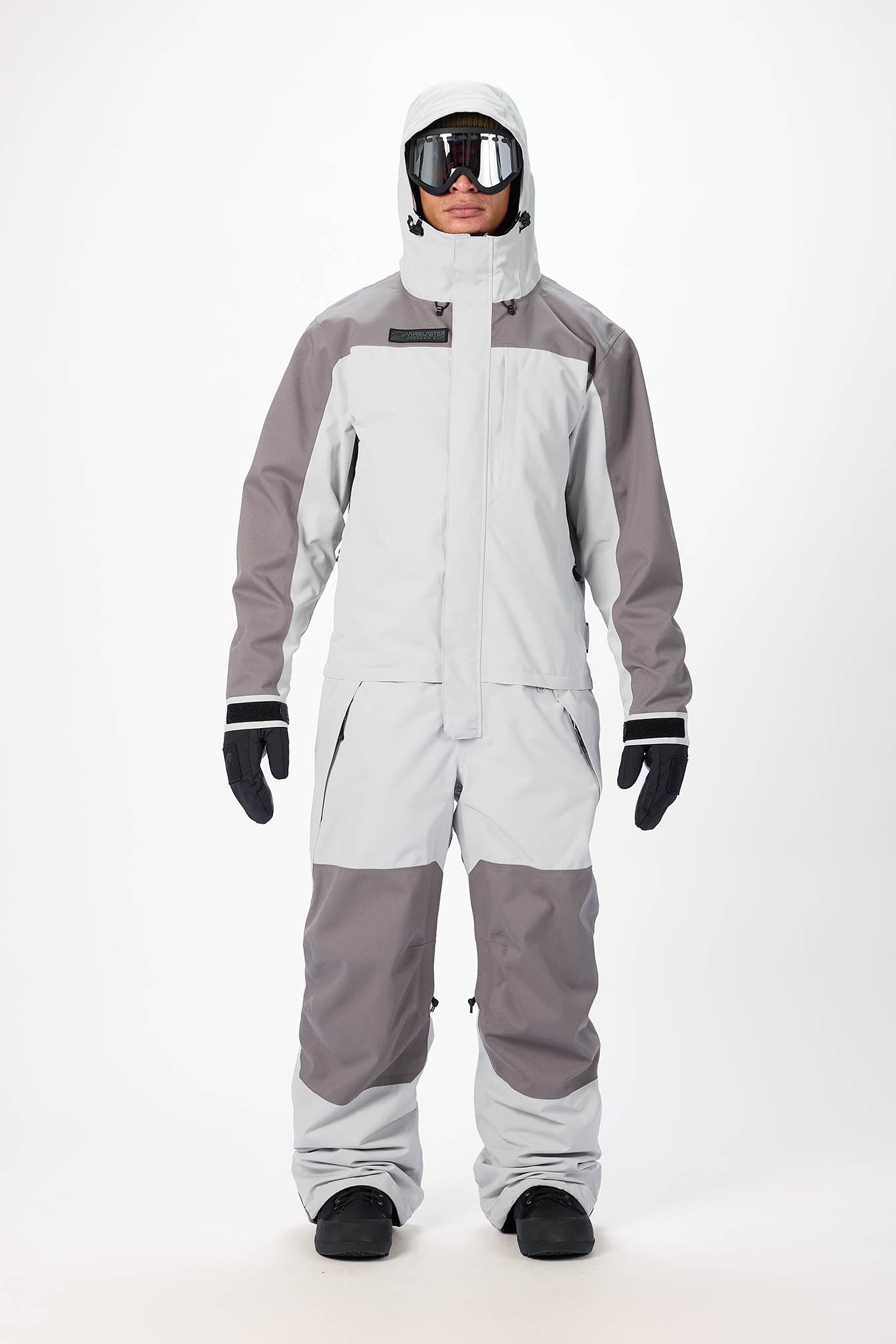 Person wearing a gray and white snowsuit with goggles on a white background