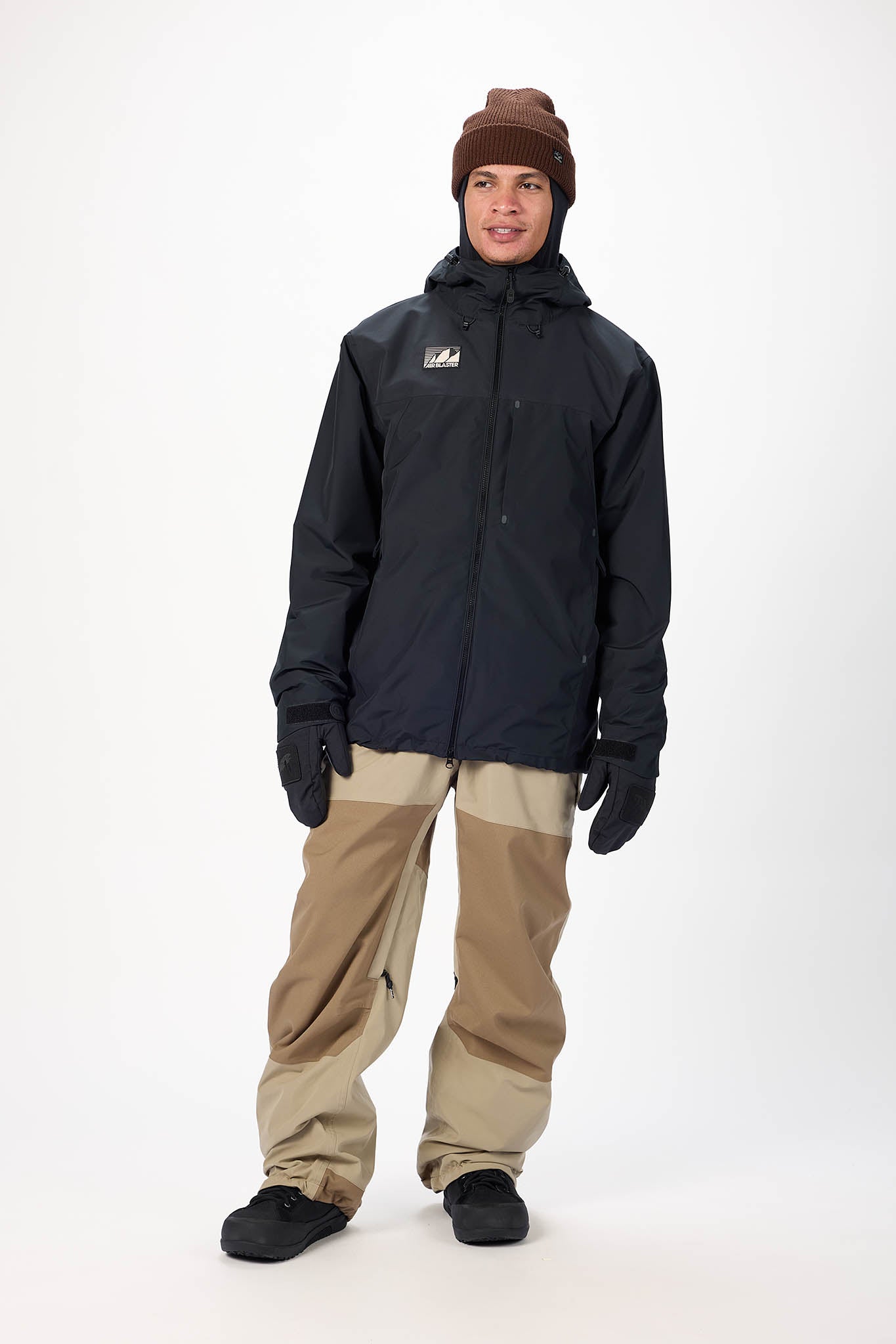 Person wearing a black jacket, beige pants, and a brown beanie on a white background