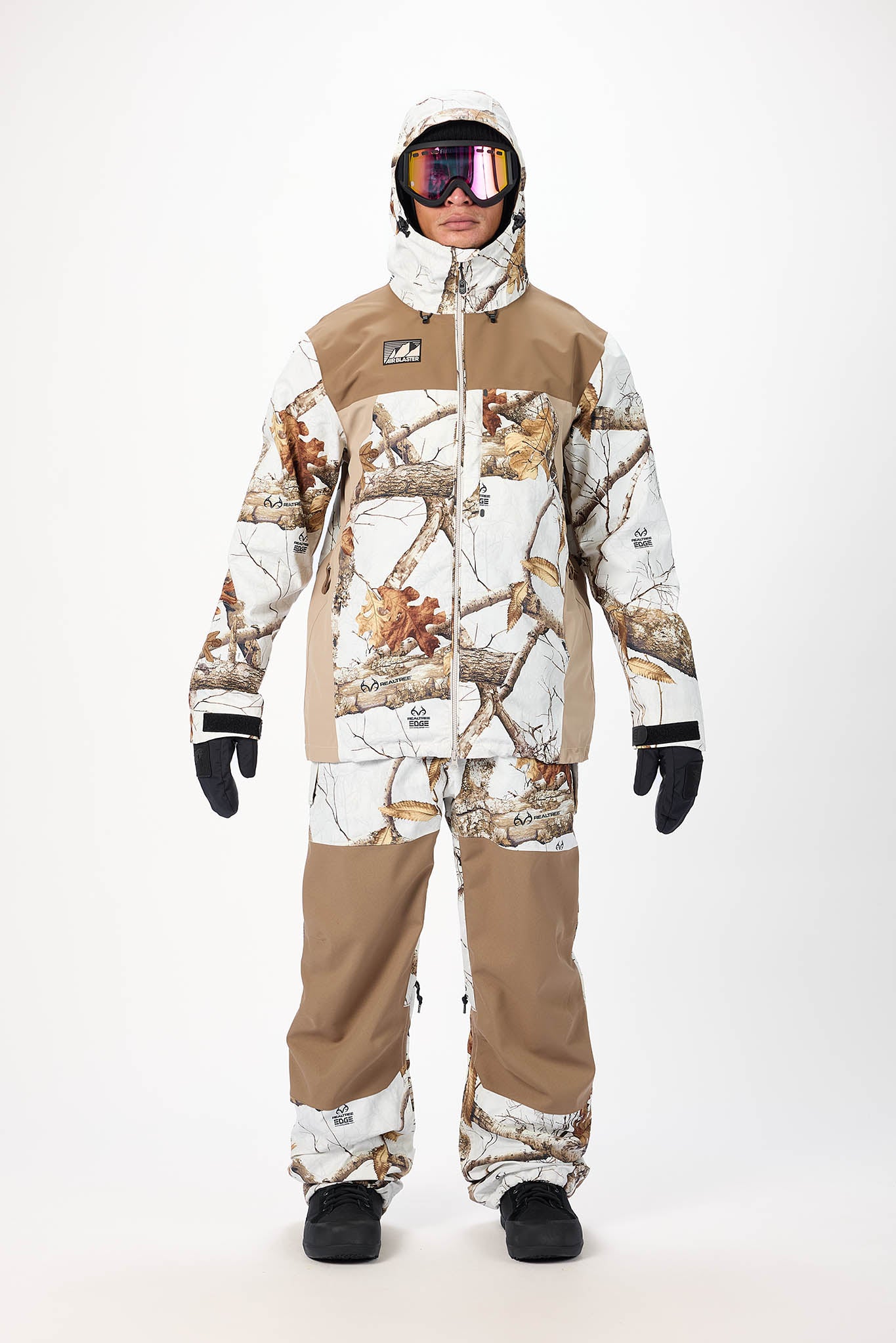 Person wearing a camouflage snowsuit with a hood, goggles, and gloves on a white background