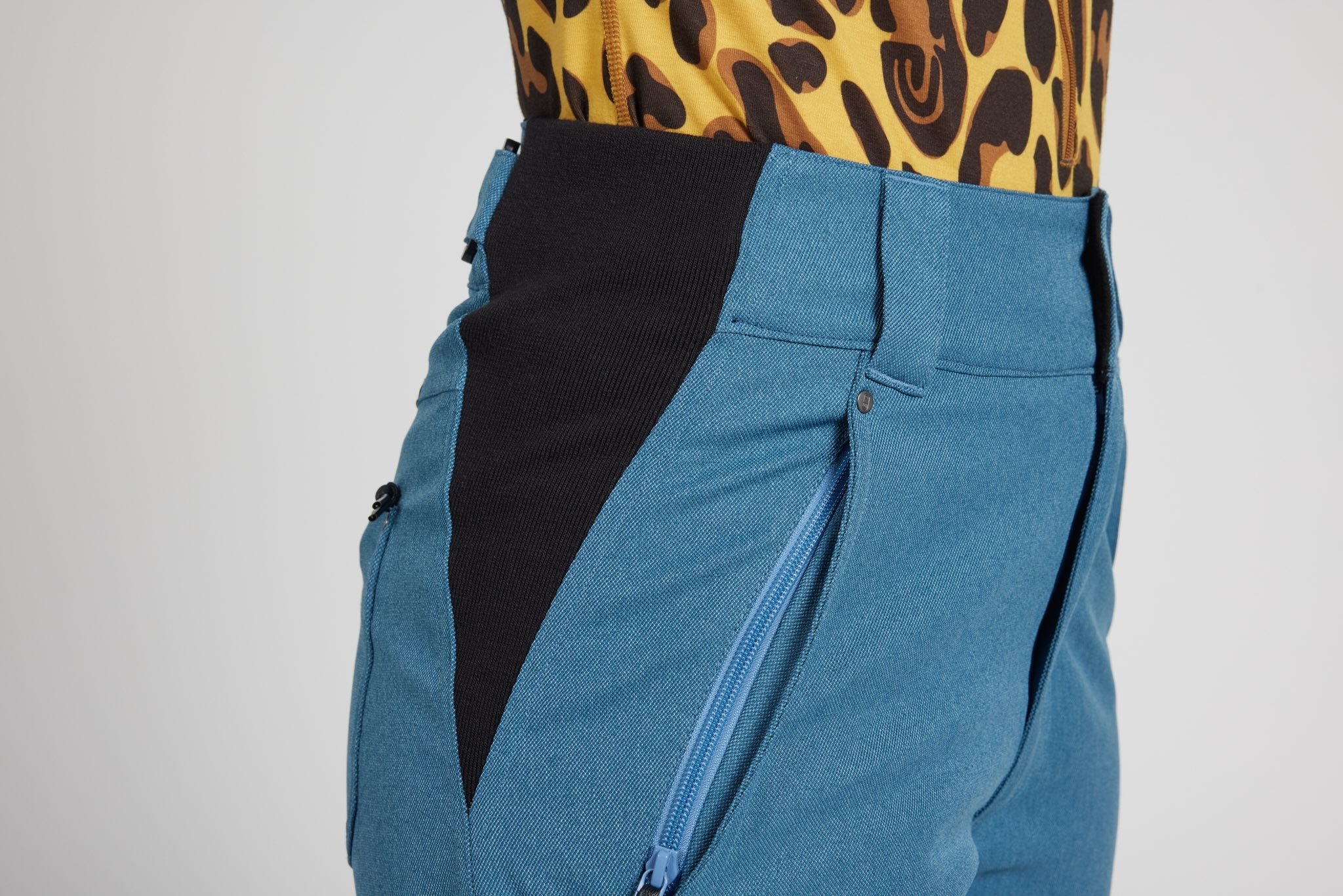 Close-up of a person wearing blue and black color-blocked pants with a leopard-print top visible at the waist, against a light gray studio background.