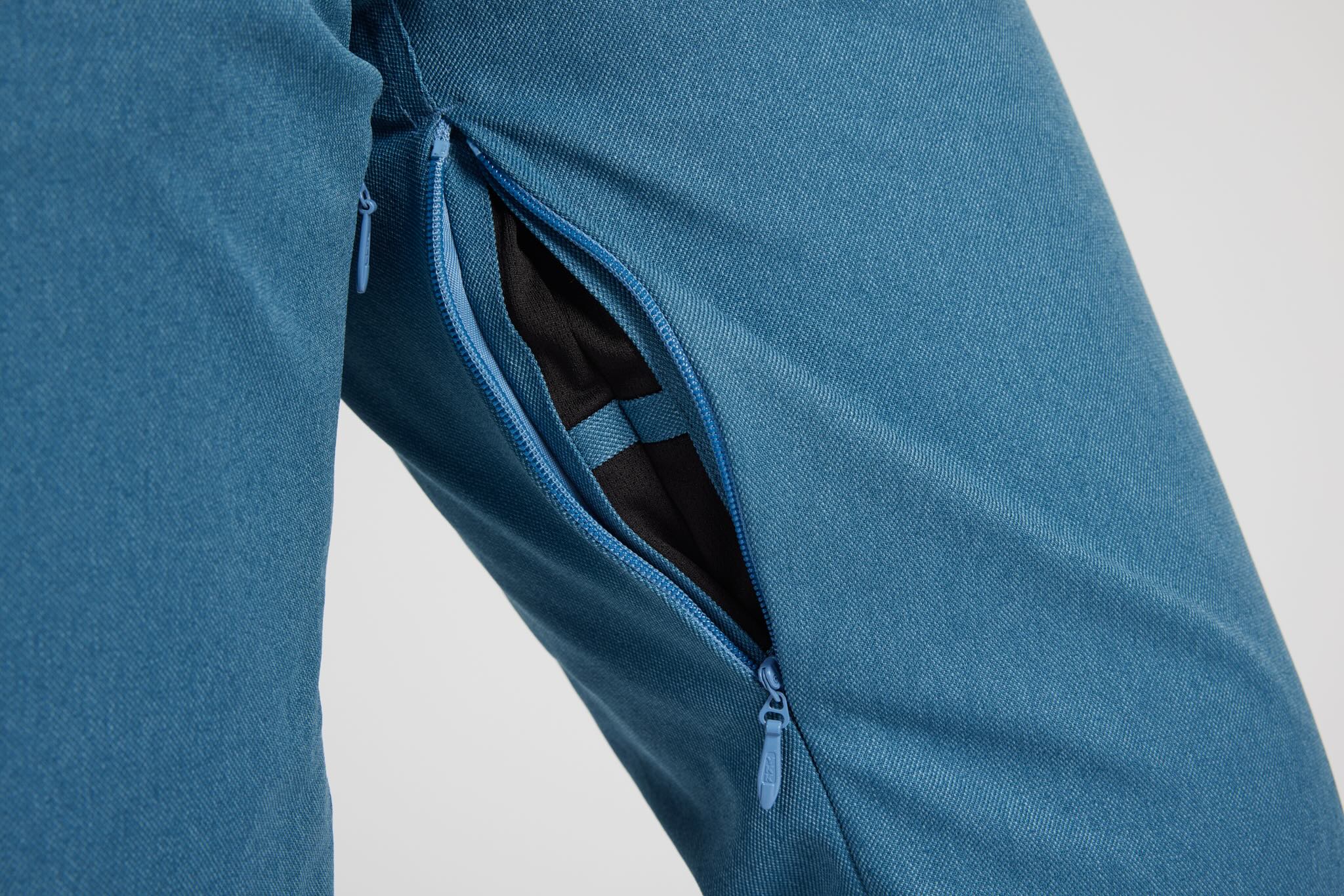 Close-up of a blue textured fabric garment with a side zipper opening, showing a black interior lining and blue zipper pull on a light gray background.