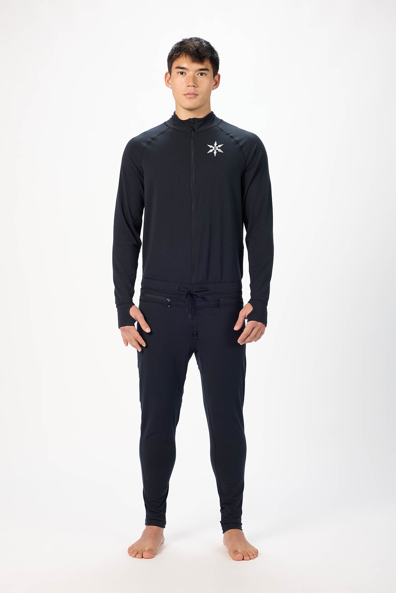 A man modeling a black long-sleeve athletic zip-up top onesie against a plain white studio background.