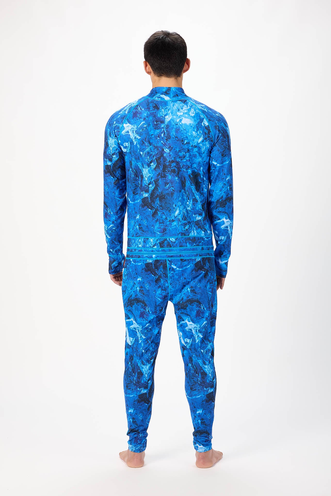 view from behind A man modeling a blue abstract pattern full-zip athletic onesie with a small white logo on the left chest, standing against a plain white studio background.