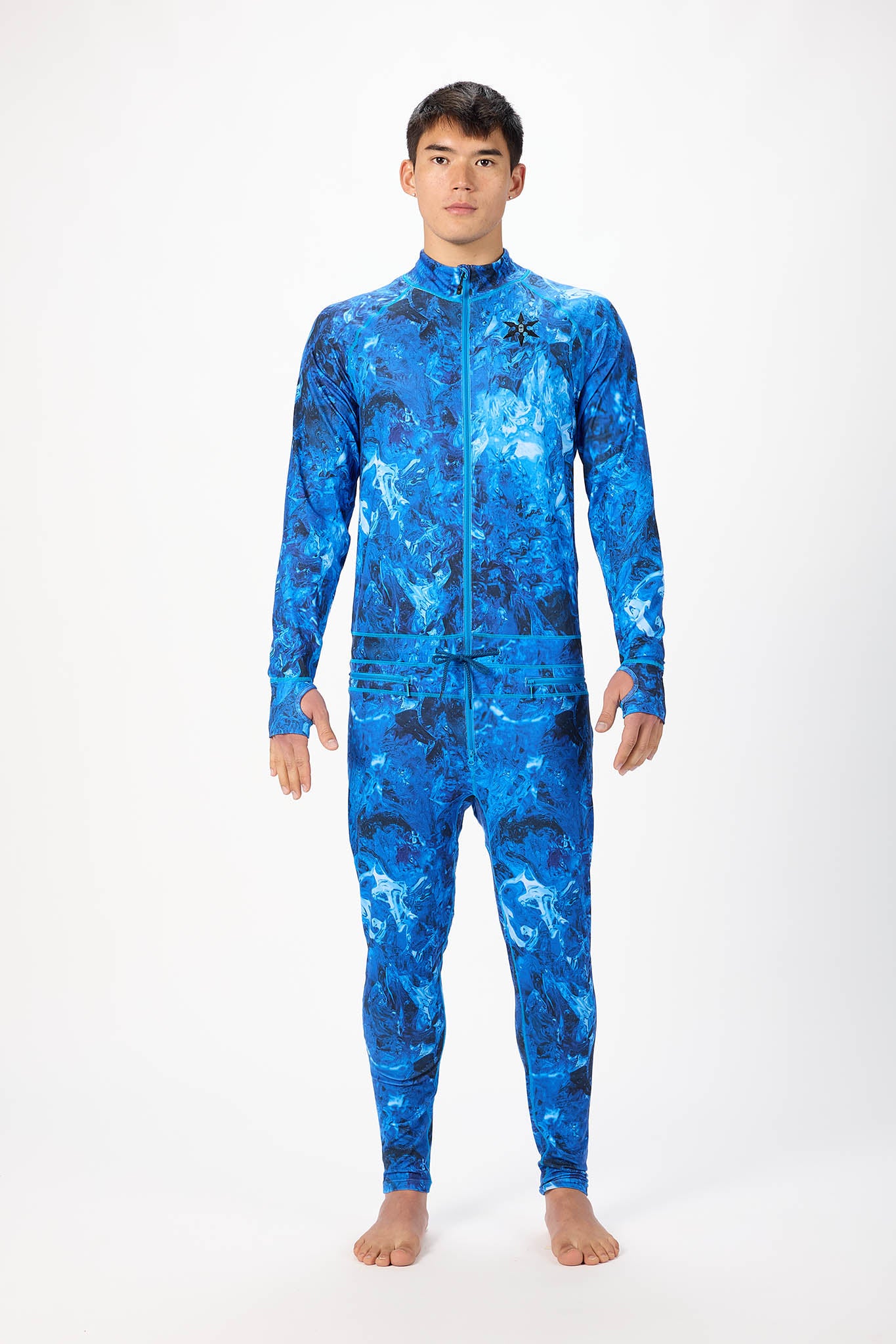 A man modeling a blue abstract pattern full-zip athletic onesie with a small white logo on the left chest, standing against a plain white studio background.