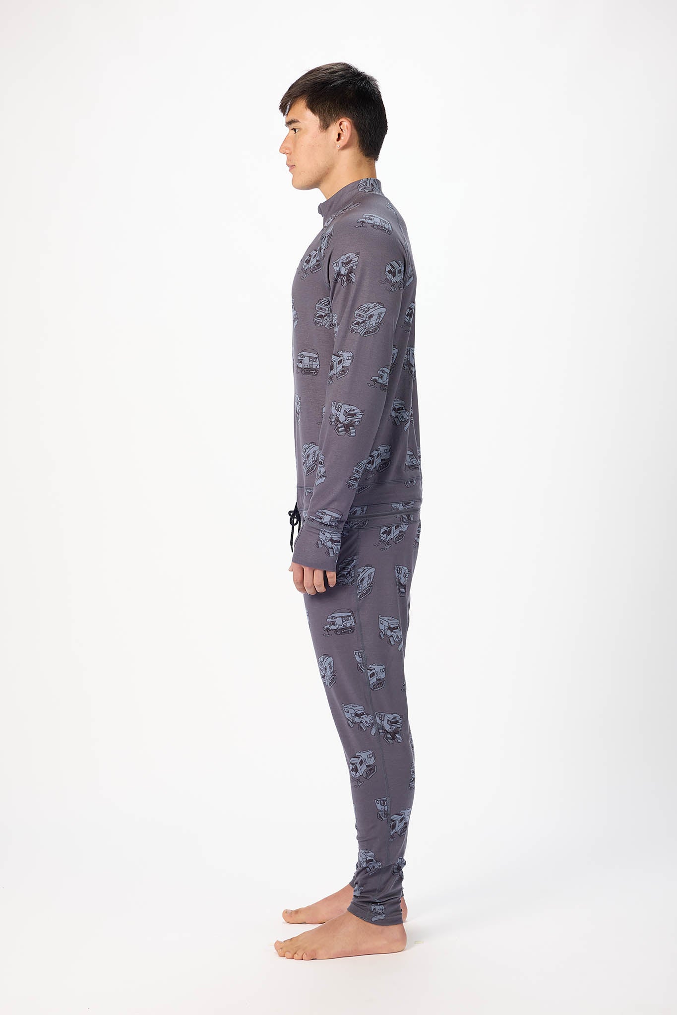 in side profile A man modeling a grey pick up truck like pattern full-zip athletic onesie with a small white logo on the left chest, standing against a plain white studio background.