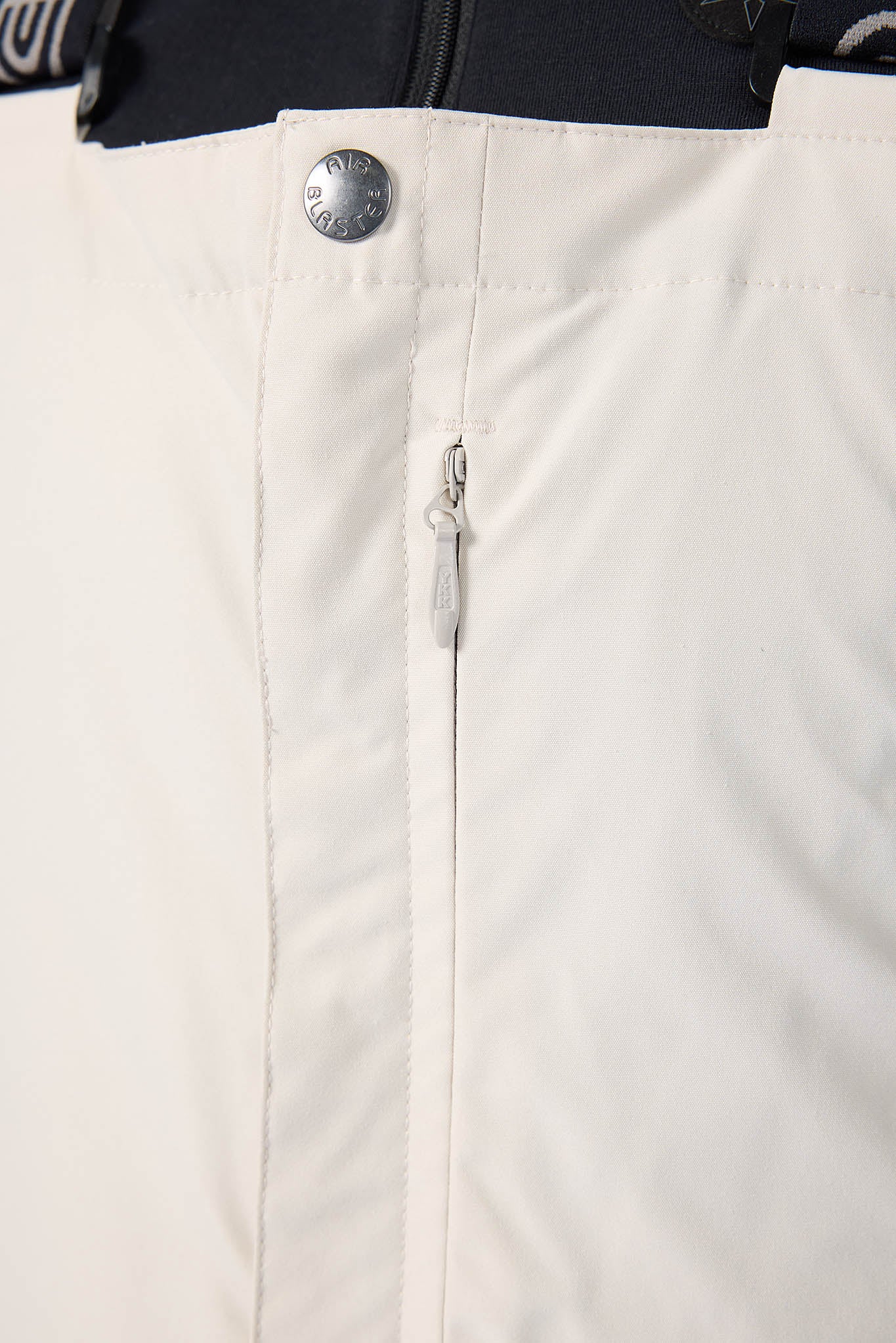 Close-up of a button on a beige jacket with a black sleeve.