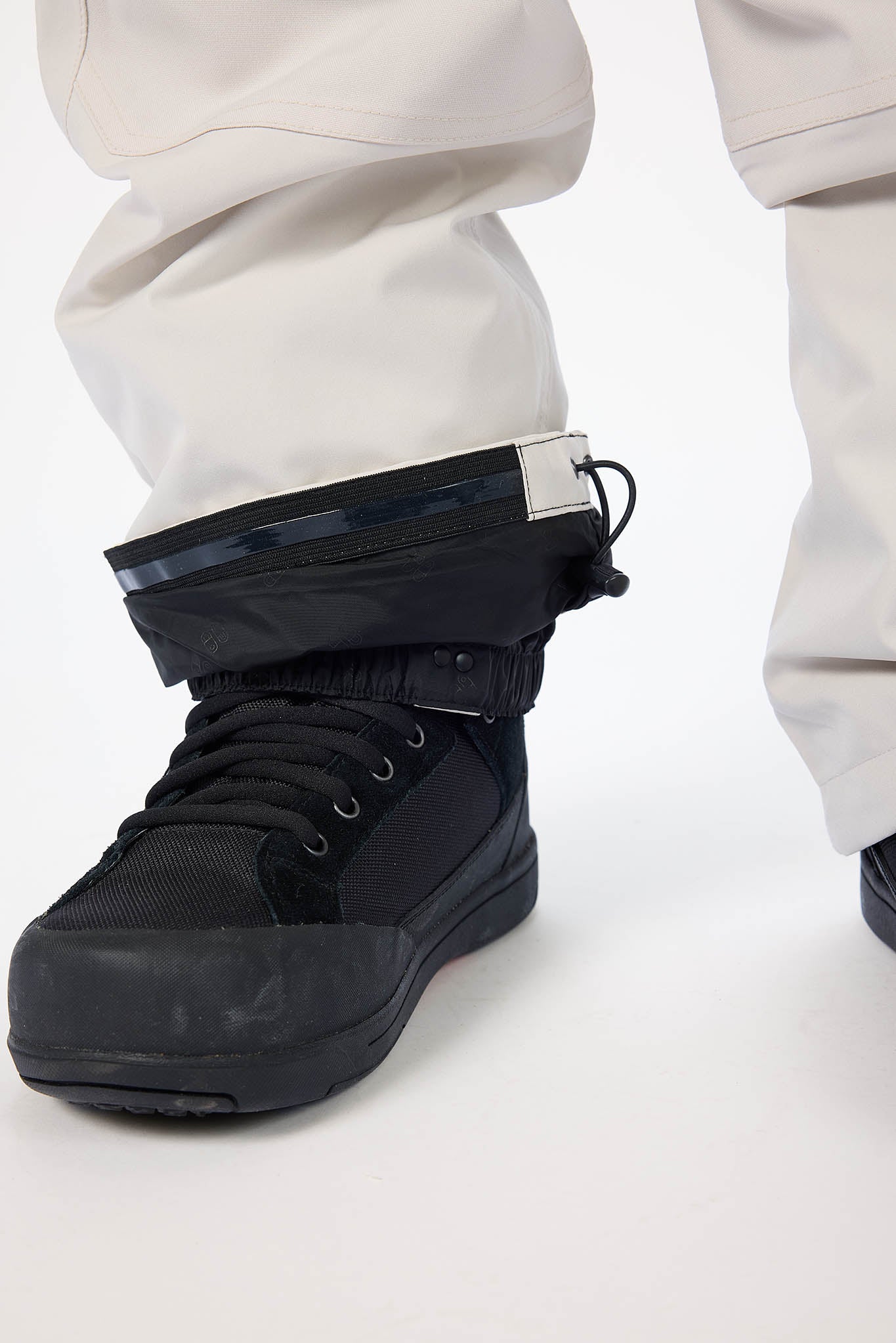 Black boot with a gaiter worn by a person on a white background
