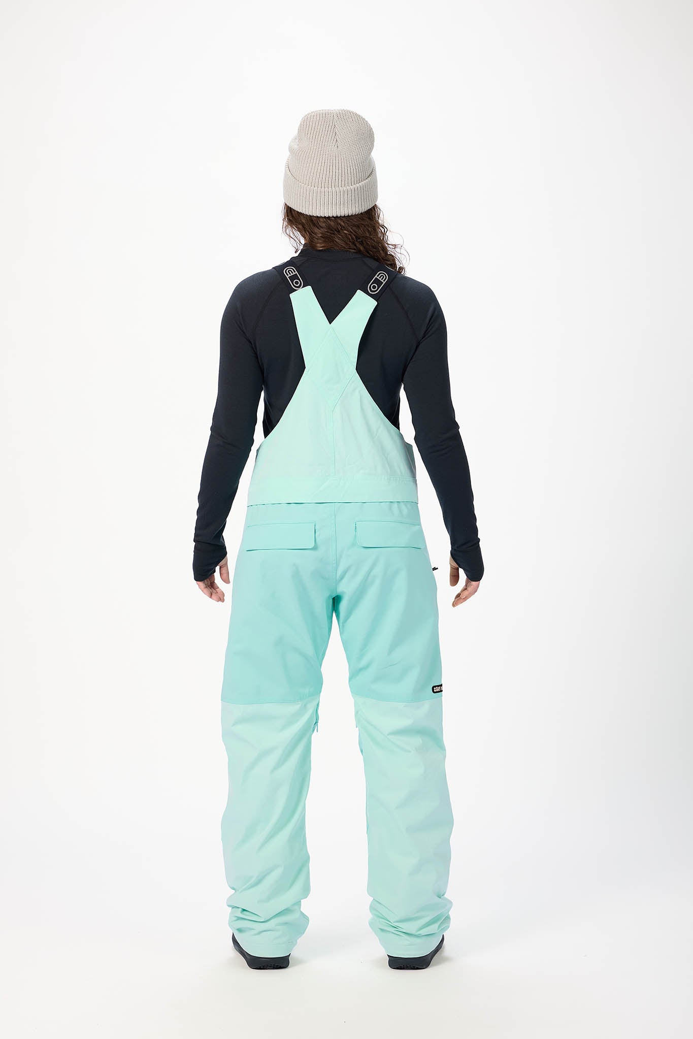 Person wearing light blue snow pants with suspenders on a white background