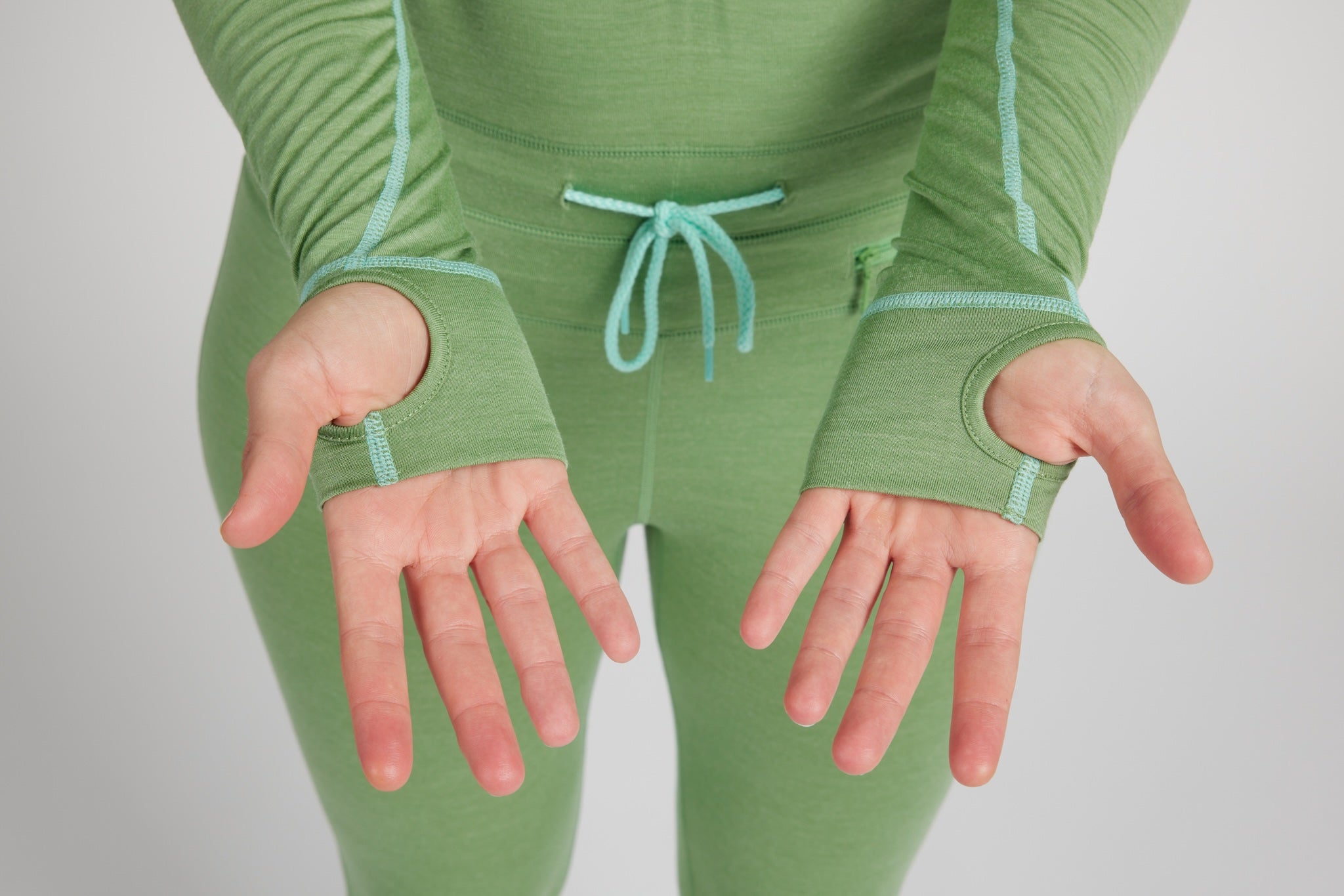 A person wearing a light green full-body knit activewear set with matching fingerless sleeves and a drawstring waist, shown against a light gray studio background.