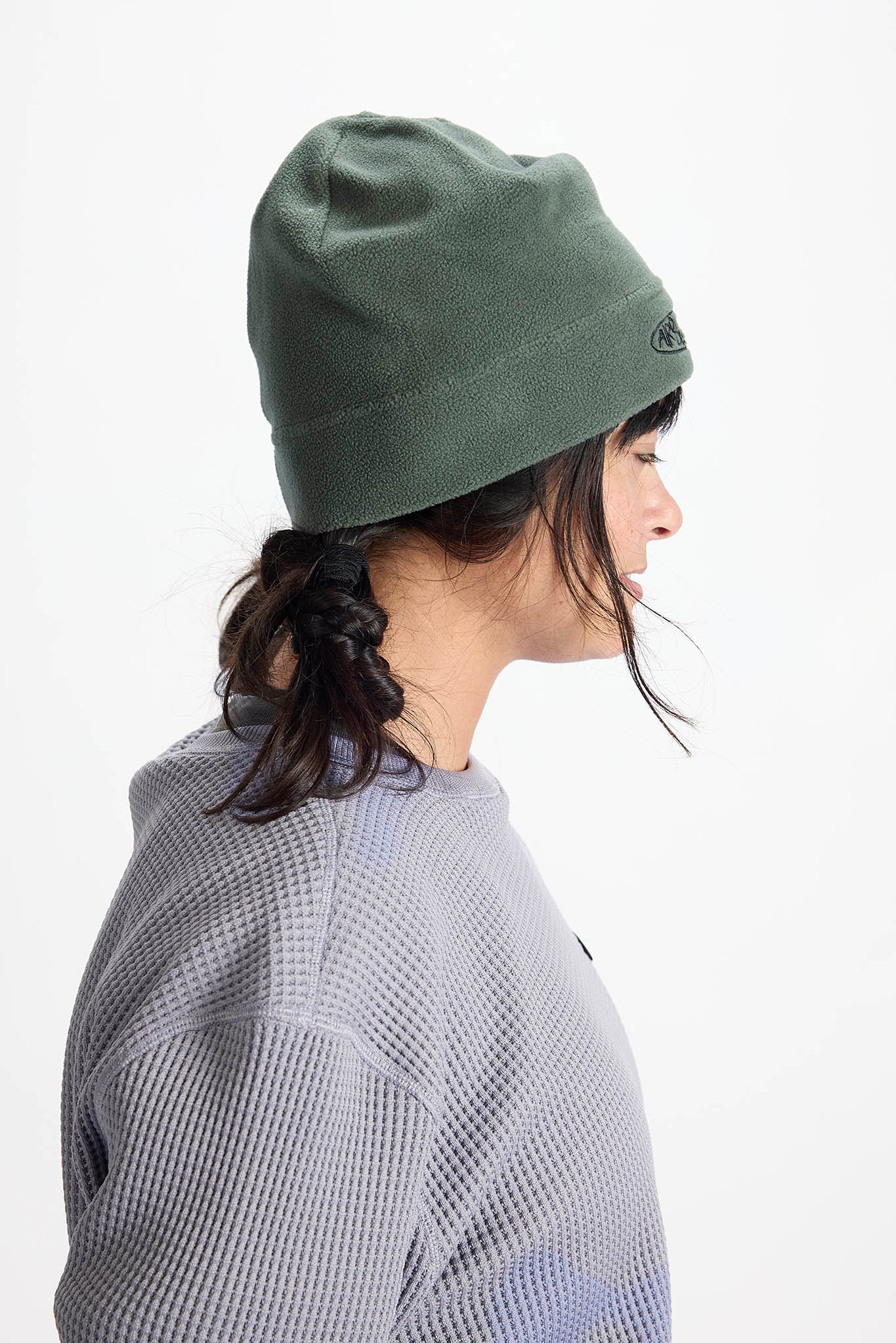 A side-profile view of a person wearing an olive green knit beanie and a gray waffle-knit sweatshirt against a plain white background.