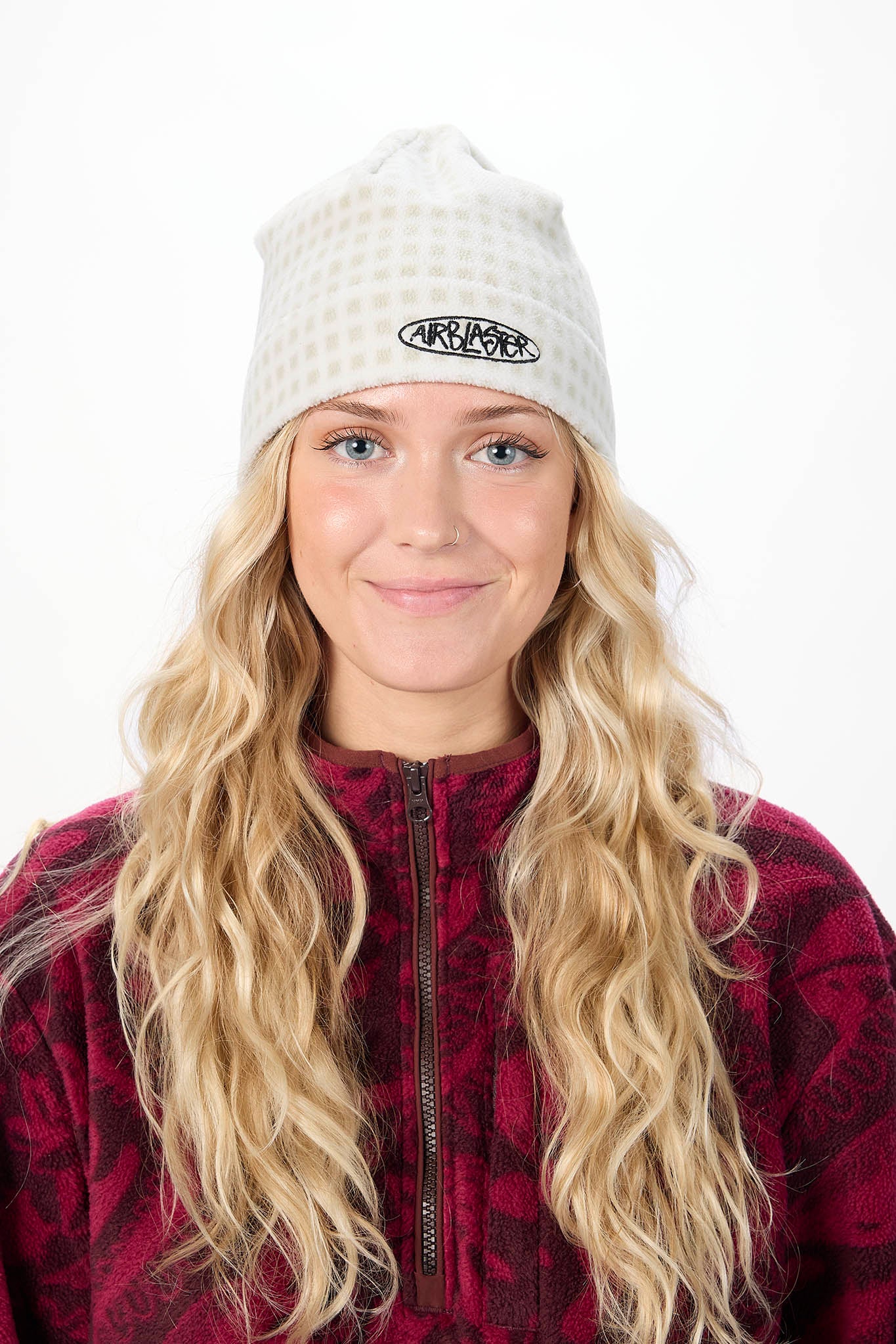 Person wearing a white knit beanie with a logo and a red plaid jacket on a white background