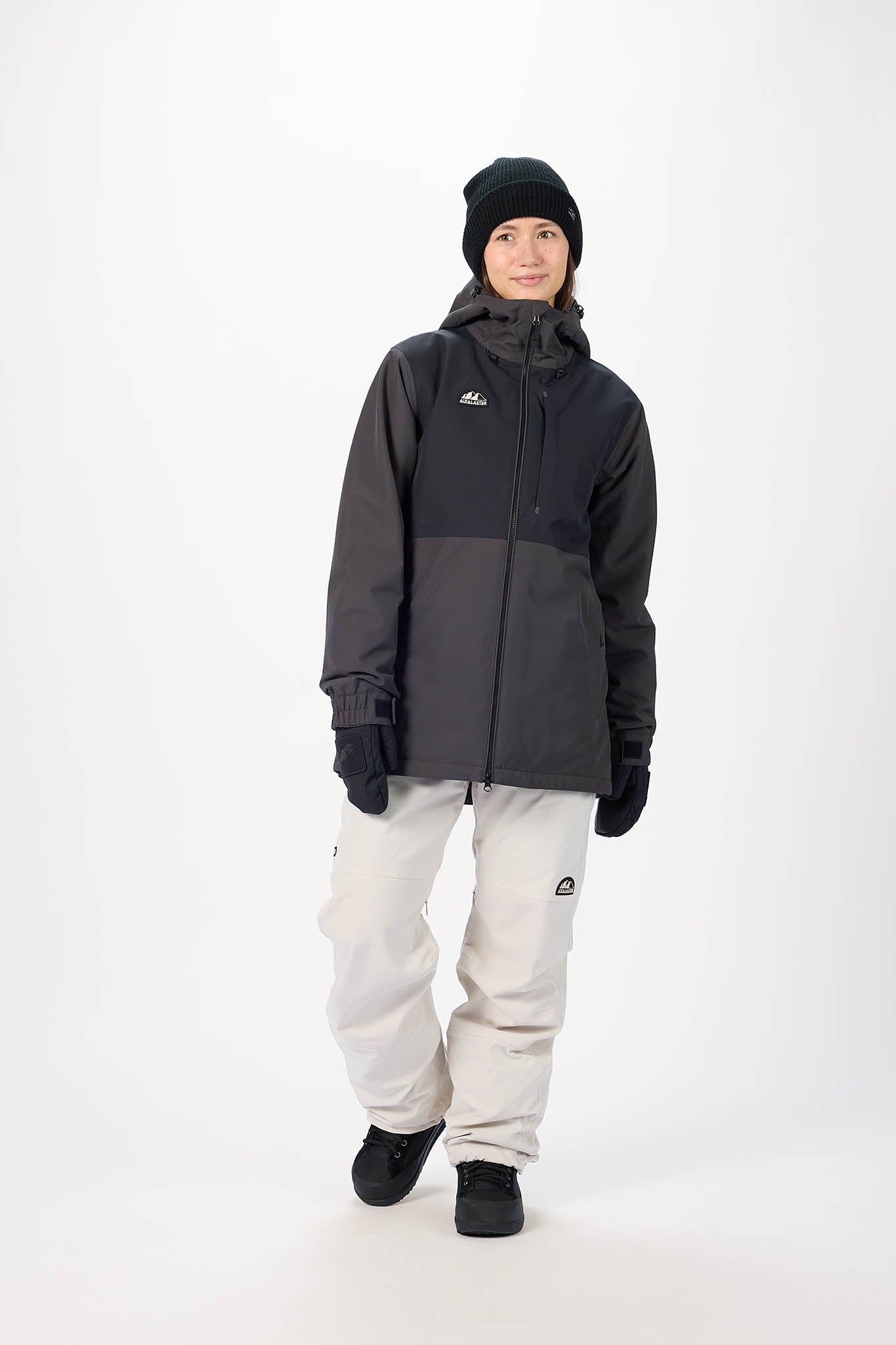 Person wearing a black and gray jacket with white pants on a white background