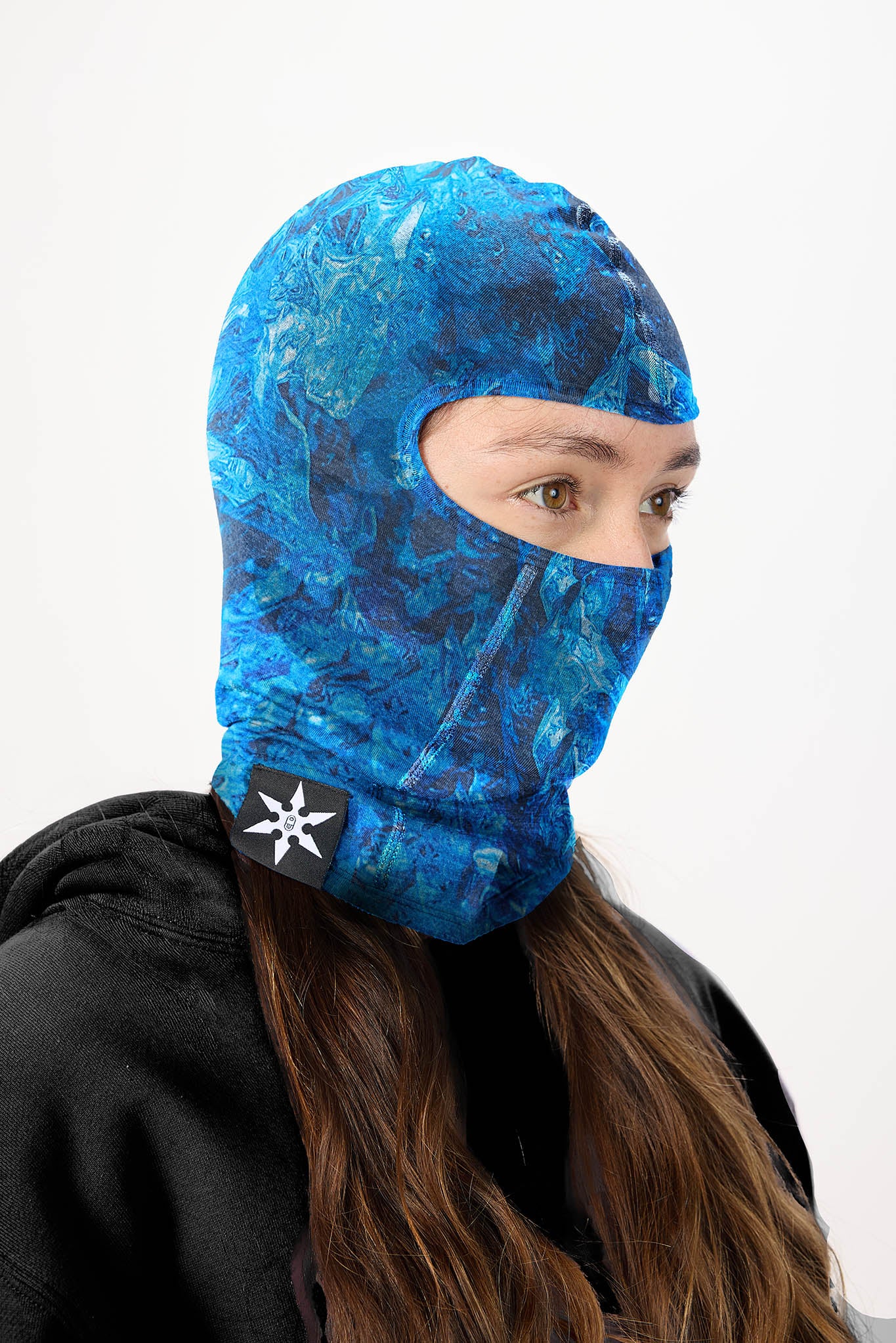 A person wearing a blue marbled patterned balaclava mask with a black chin strap featuring a white logo, paired with a black hoodie against a plain white background.