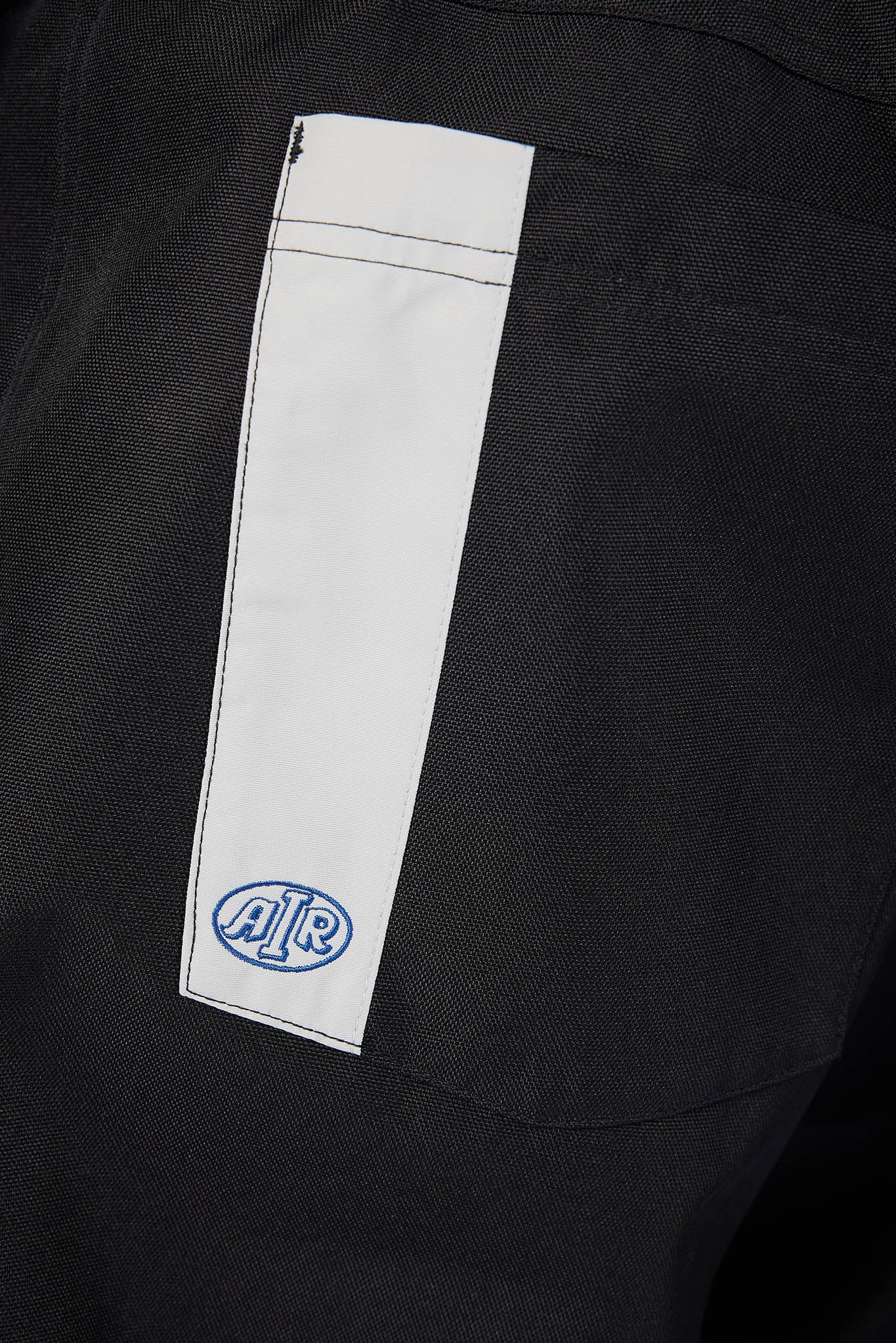 Close-up of a black textured garment with a white vertical patch on the side featuring a blue circular 'AIR' logo.