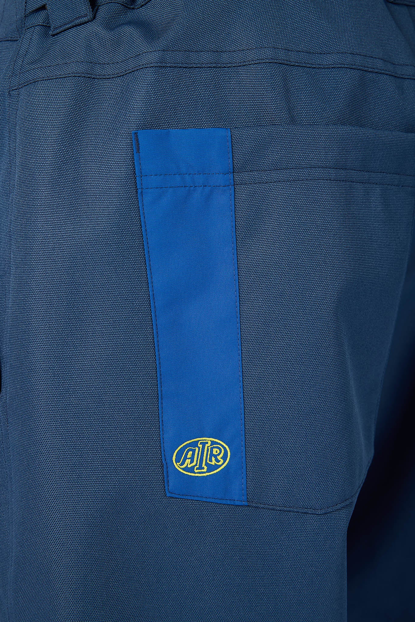 Close-up of a blue workwear jacket or pants showing a vertical bright blue pocket tab with a yellow and blue circular J.R.