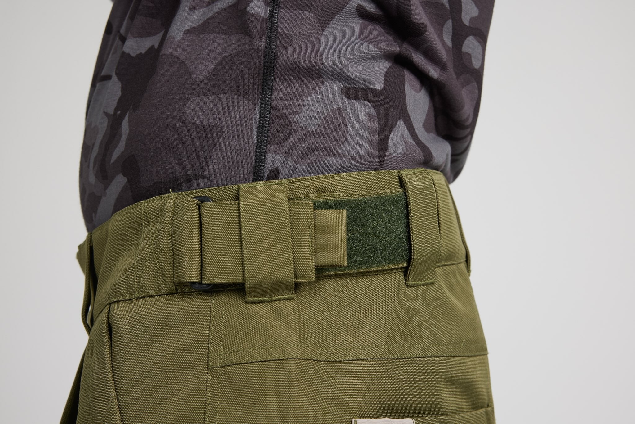 Close-up of a person wearing olive green tactical pants with a belt and a dark gray