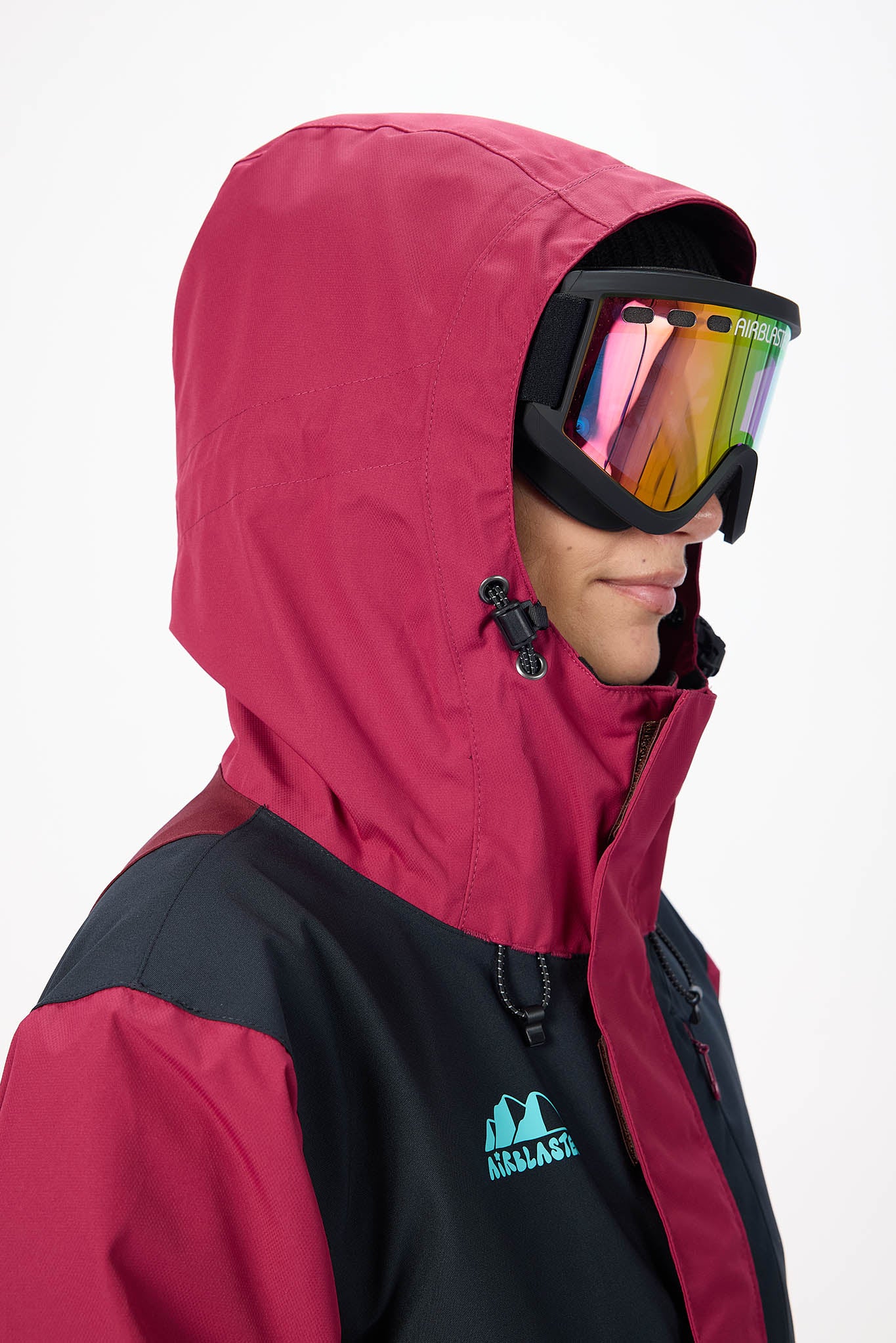 Person wearing a red and black jacket with a hood, holding colorful goggles.