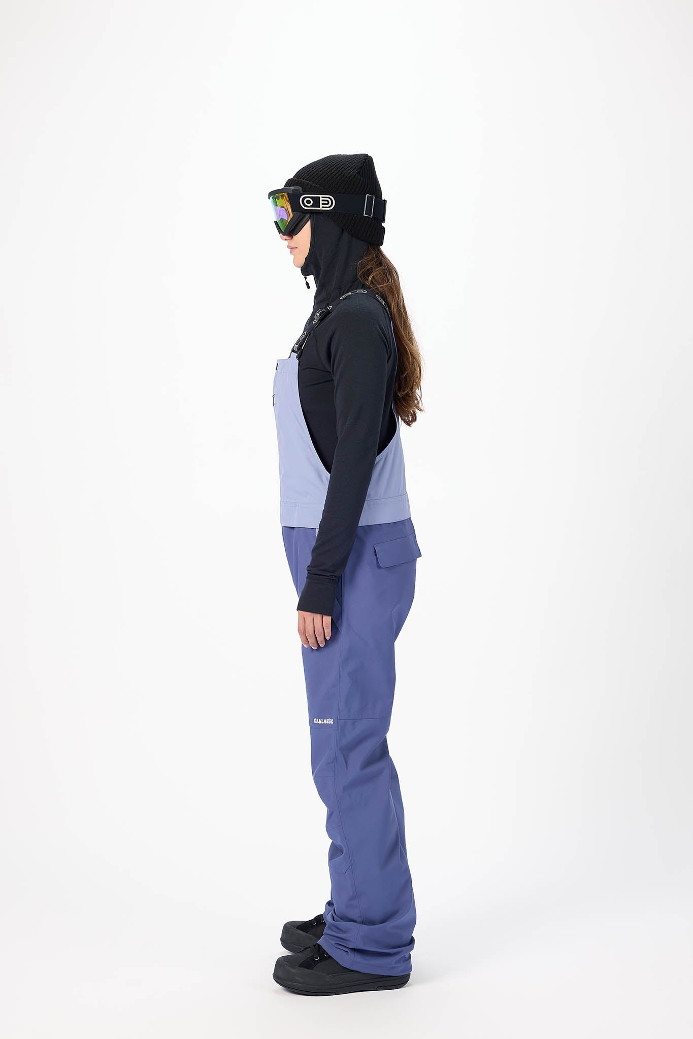 Person wearing a black jacket, blue pants, and a black beanie with colorful accents on a white background