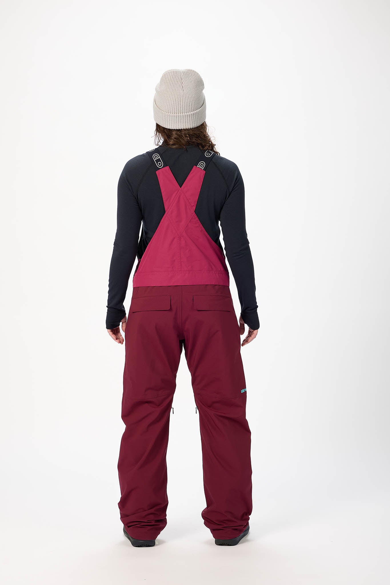 Person wearing a black long-sleeve shirt and red bib overalls on a white background