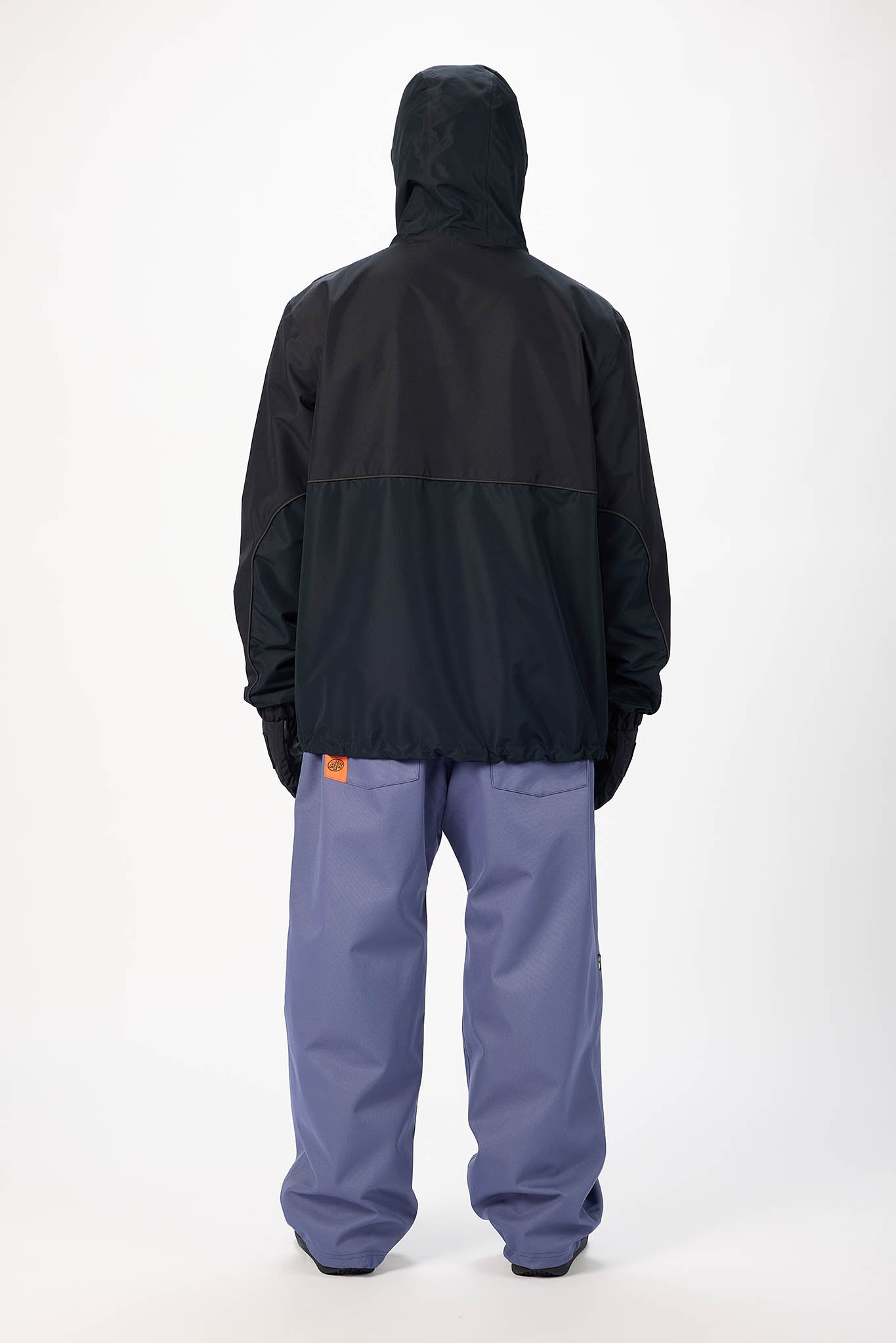 A person shown from the back wearing a black hooded jacket and slate blue pants against a plain light gray studio background.